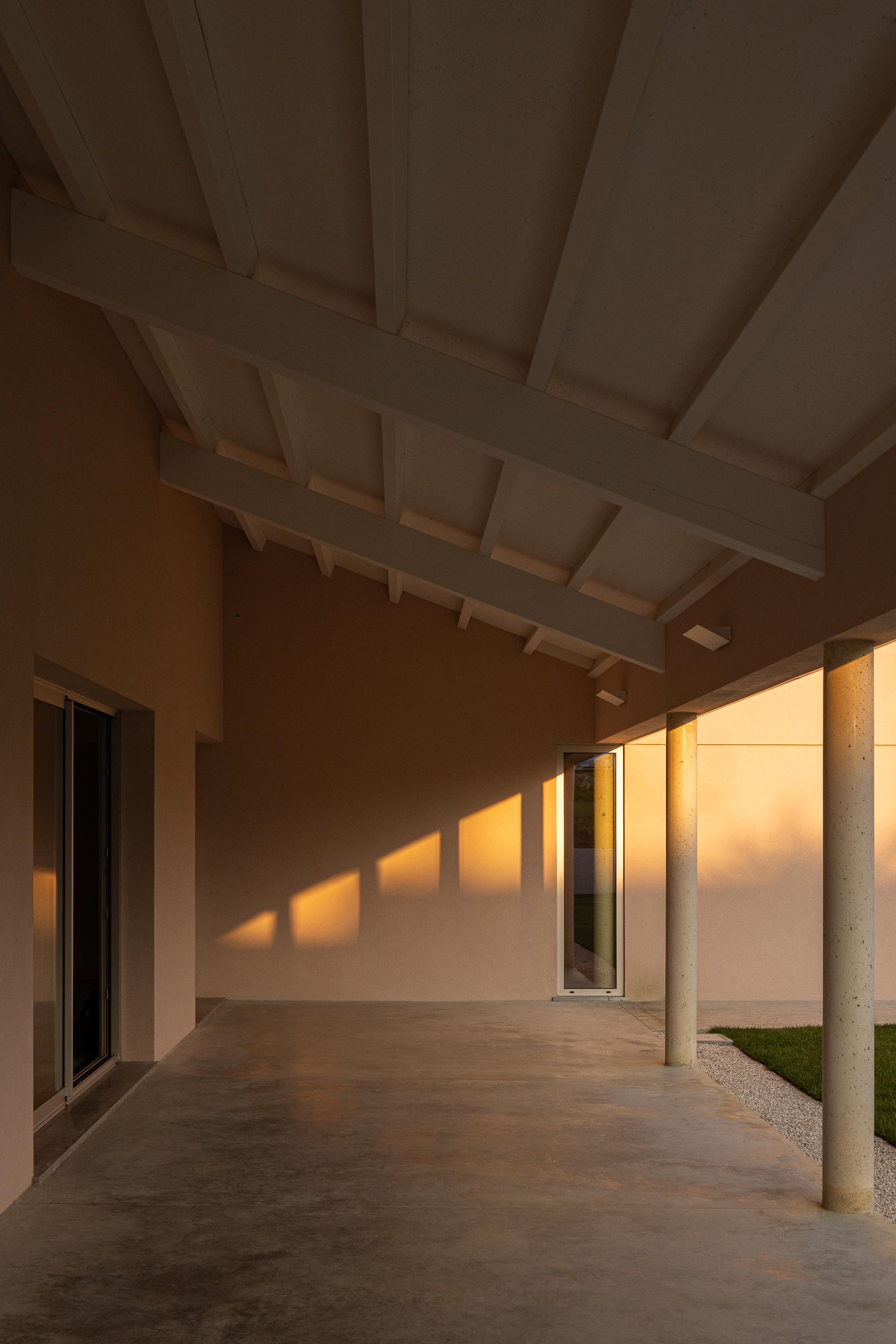 Interior do alpendre com estrutura de madeira exposta e pavimento em betão, sob luz do pôr do sol — Casa do Alpendre arquitectura Vasco Burnay Arquitectura fotografia Ivo Tavares
