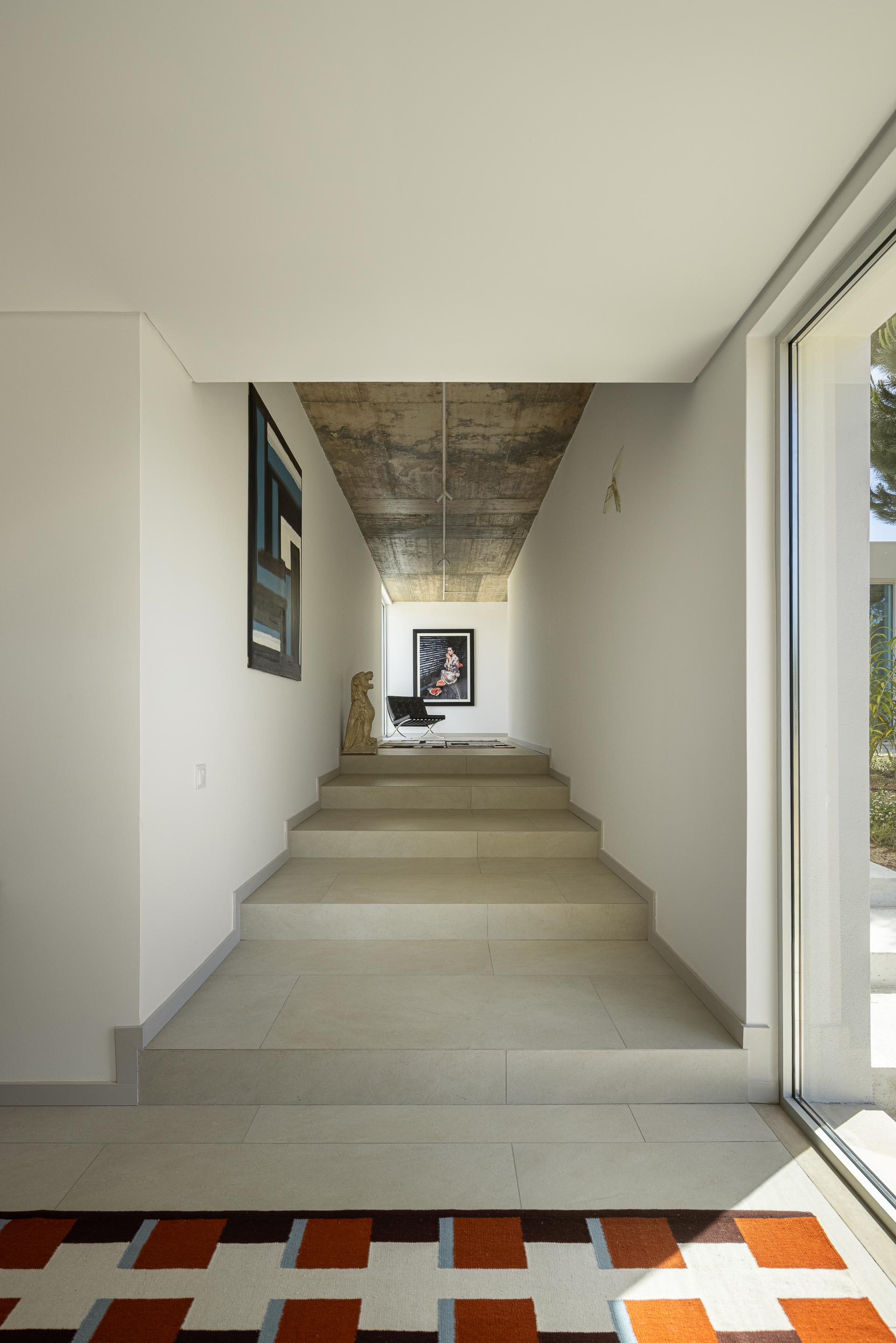 Escada interior com degraus em cerâmica clara e paredes brancas, sob cobertura em betão aparente, com luz natural — Casa M Ariane fotografia Ivo Tavares