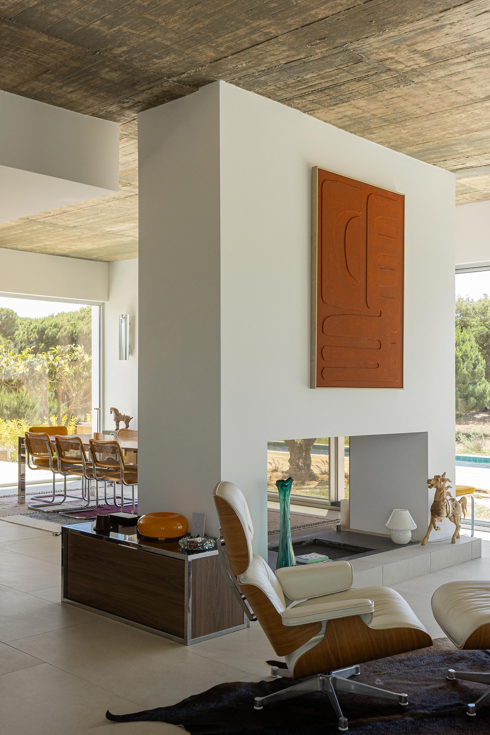 Sala de estar e jantar em planta aberta com pavimento claro, cobertura em betão aparente e lareira central — Casa M Ariane fotografia Ivo Tavares