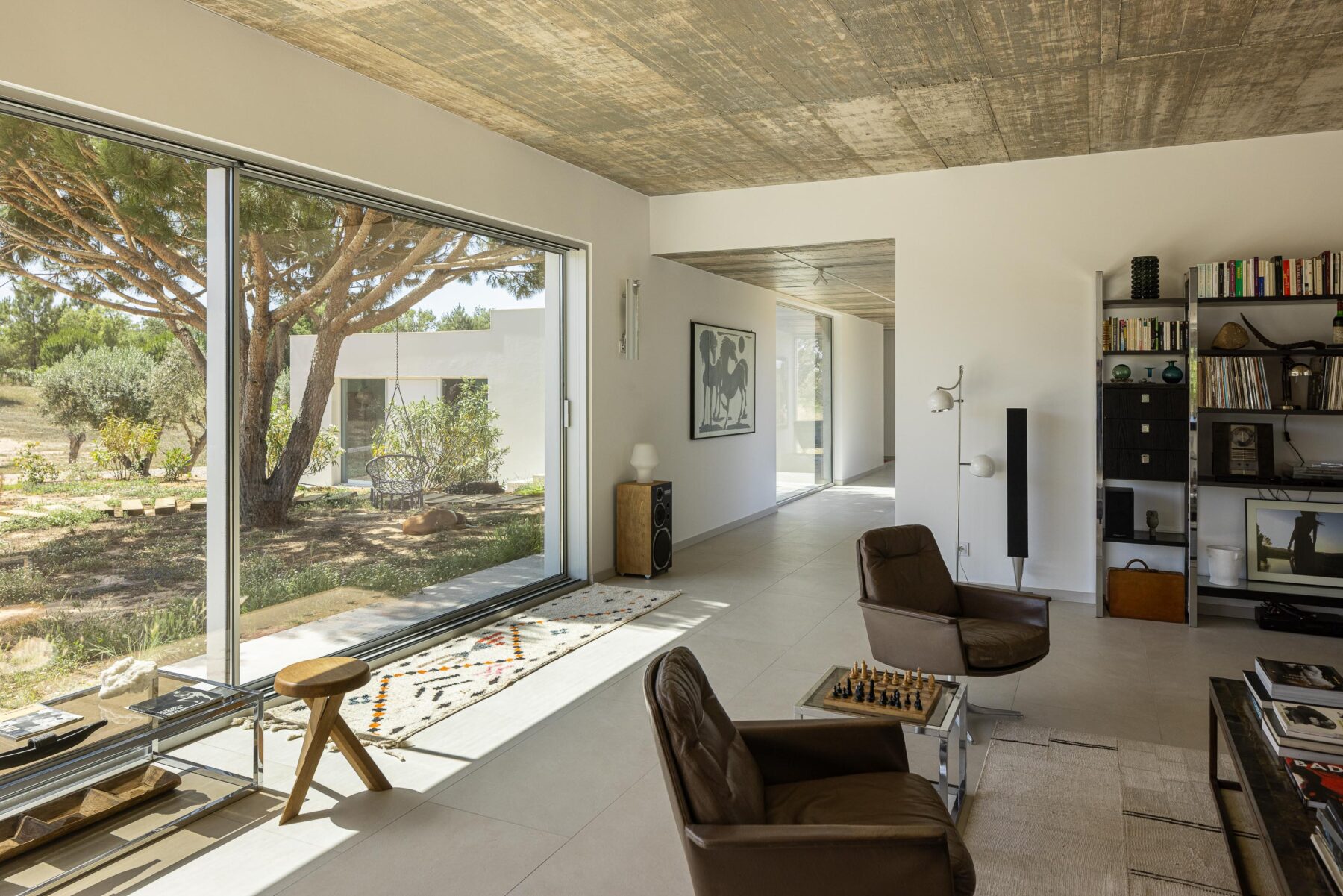 Sala de estar com pavimento em cerâmica clara, cobertura em betão aparente e grandes vãos com vista para o jardim — Casa M Ariane fotografia Ivo Tavares