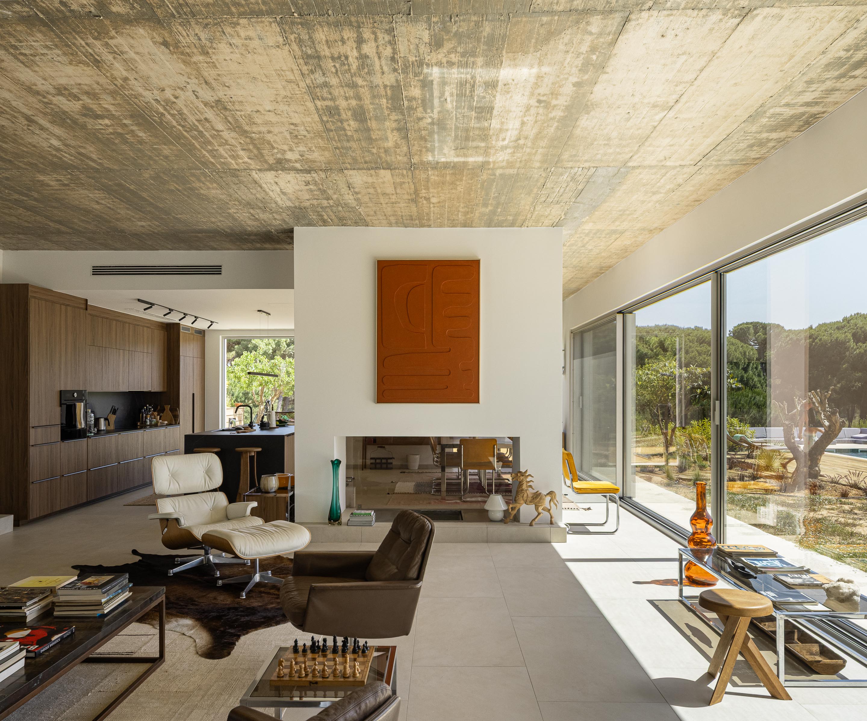Sala de estar e cozinha em planta aberta com pavimento claro, cobertura em betão aparente e grandes vãos envidraçados — Casa M Ariane fotografia Ivo Tavares