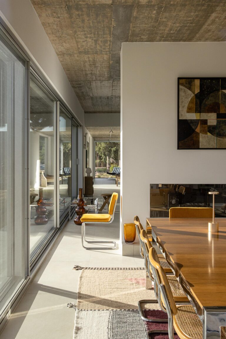 Sala de jantar com pavimento claro, cobertura em betão aparente e grandes vãos envidraçados, com vista para o exterior — Casa M Ariane fotografia Ivo Tavares