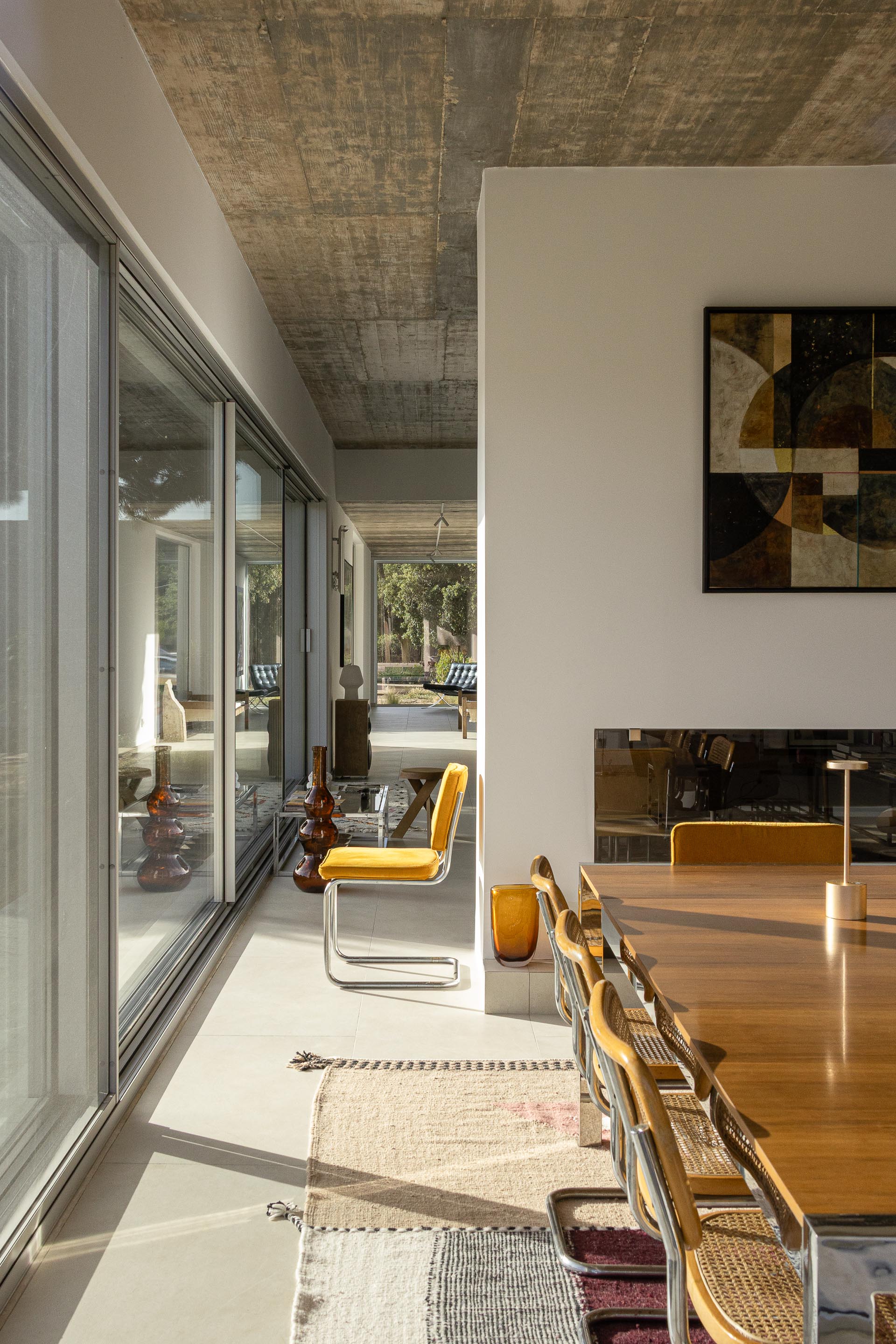 Sala de jantar com pavimento claro, cobertura em betão aparente e grandes vãos envidraçados, com vista para o exterior — Casa M Ariane fotografia Ivo Tavares