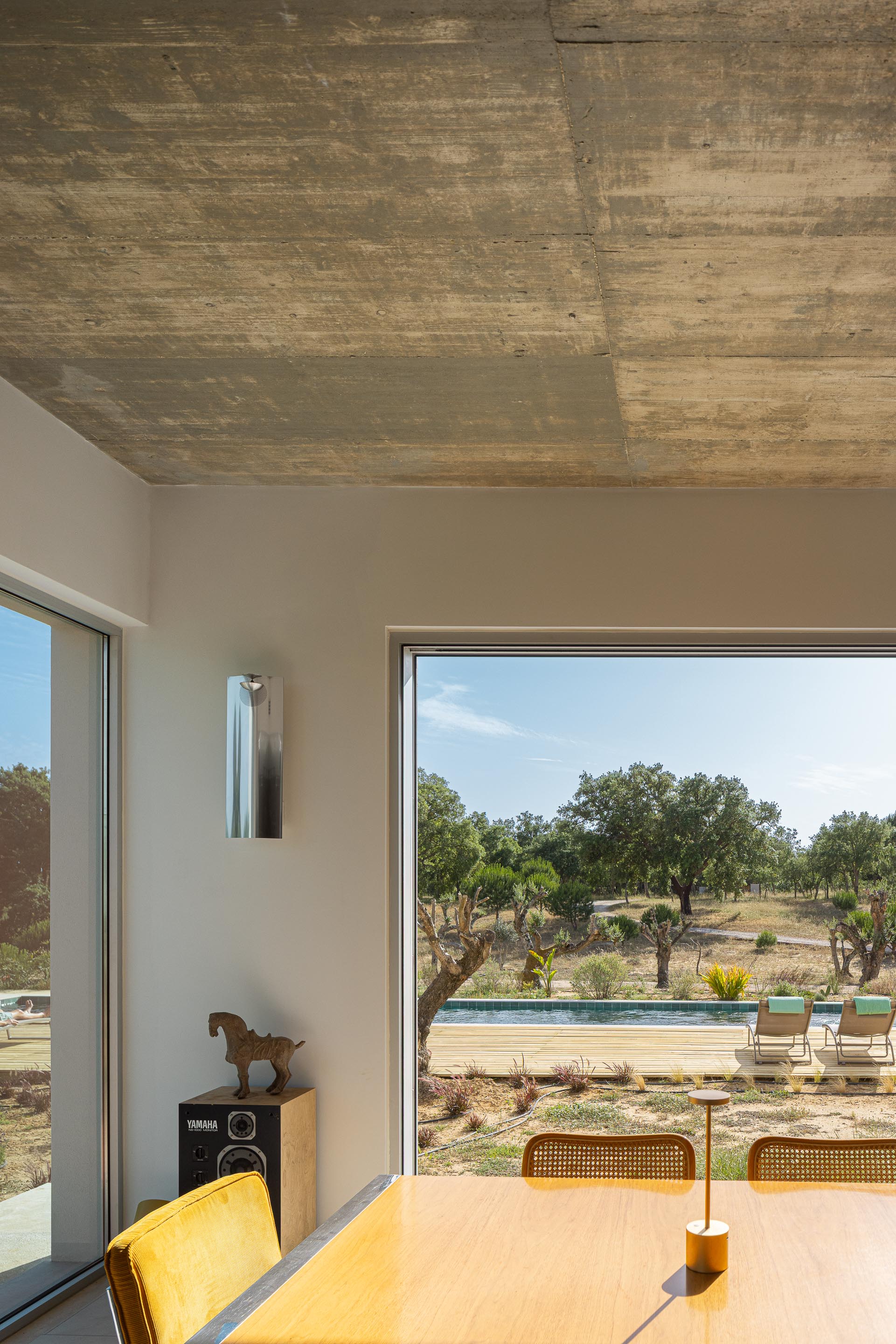 Sala de jantar com pavimento claro e cobertura em betão aparente, com vista para a piscina e a paisagem natural — Casa M Ariane fotografia Ivo Tavares