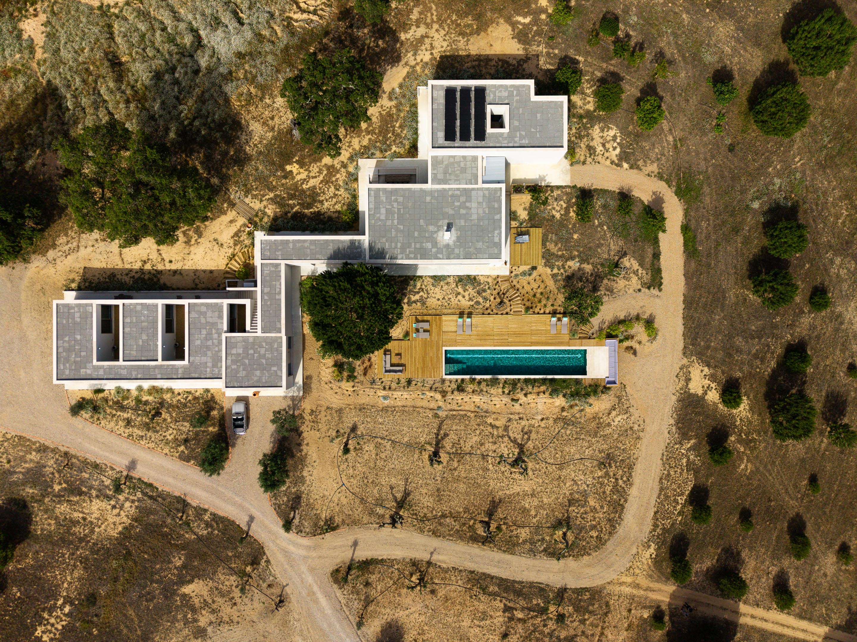 Vista aérea da moradia em planta L com coberturas planas, piscina e deck em madeira, integrada na paisagem árida — Casa M Ariane fotografia Ivo Tavares
