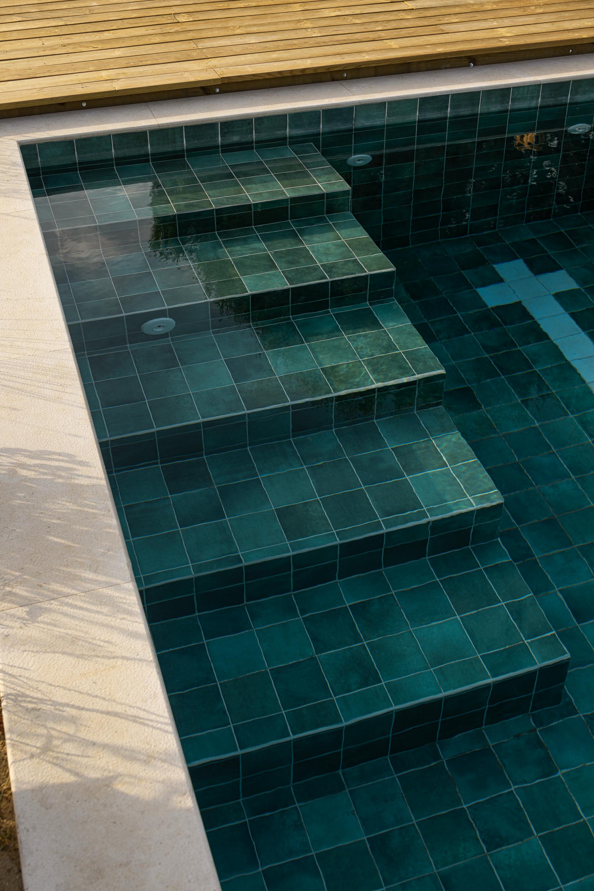 Detalhe da piscina com revestimento em azulejo verde-azulado e degraus submersos, com bordadura em pedra branca — Casa M Ariane fotografia Ivo Tavares