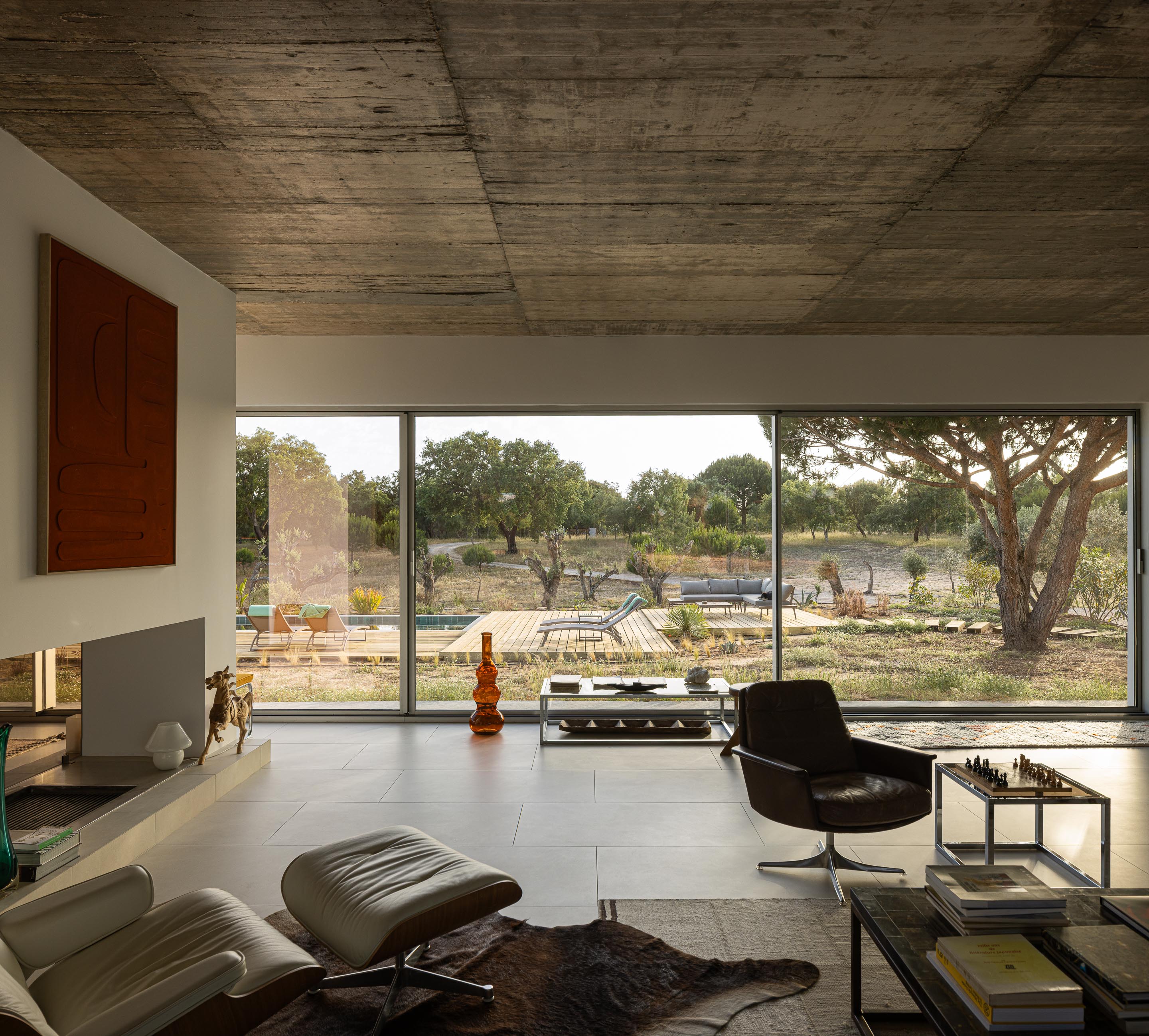 Sala de estar com pavimento claro, cobertura em betão aparente e grandes vãos com vista para a piscina e paisagem — Casa M Ariane fotografia Ivo Tavares