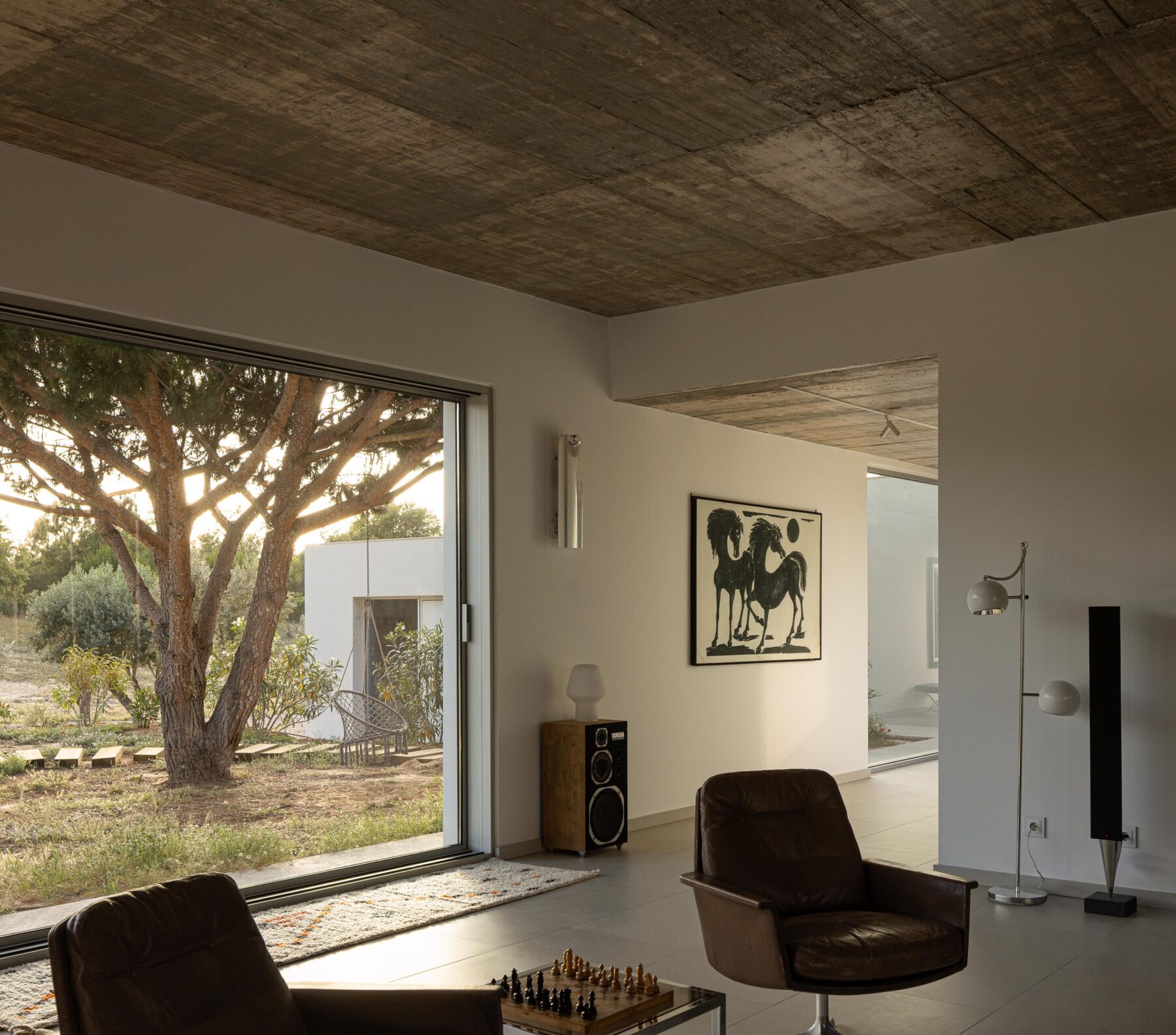 Sala de estar com pavimento claro, cobertura em betão aparente e grandes vãos com vista para o jardim exterior — Casa M Ariane fotografia Ivo Tavares