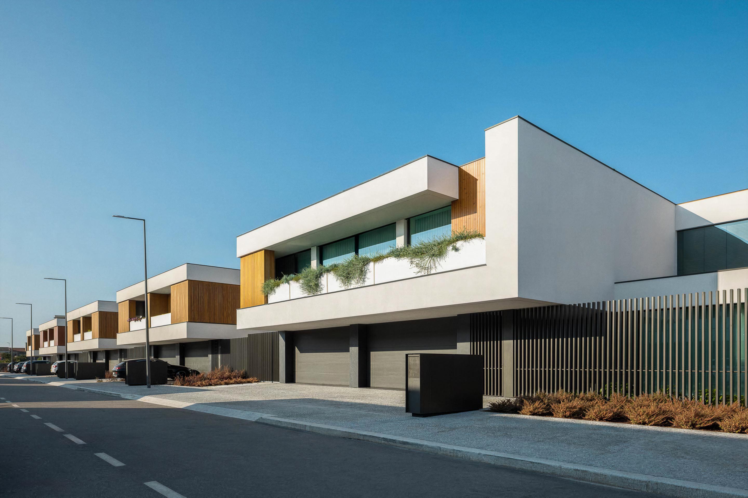 Fachada da moradia com volumes brancos, revestimento em madeira mel e varandas com vegetação — Casa FJ arquitectura MIL870 + GRAUON fotografia Ivo Tavares