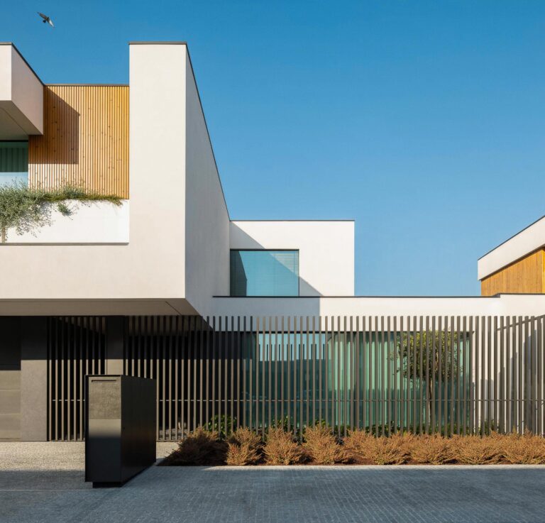 Fachada da moradia com volumes brancos, painéis de madeira mel e vedação vertical em metal cinzento — Casa FJ arquitectura MIL870 + GRAUON fotografia Ivo Tavares