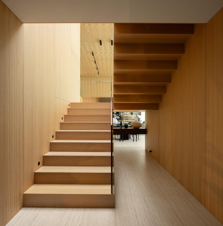 Escadaria com degraus e paredes em madeira mel, guarda-corpos em vidro estrutural e pavimento em pedra clara — Casa FJ arquitectura MIL870 + GRAUON fotografia Ivo Tavares
