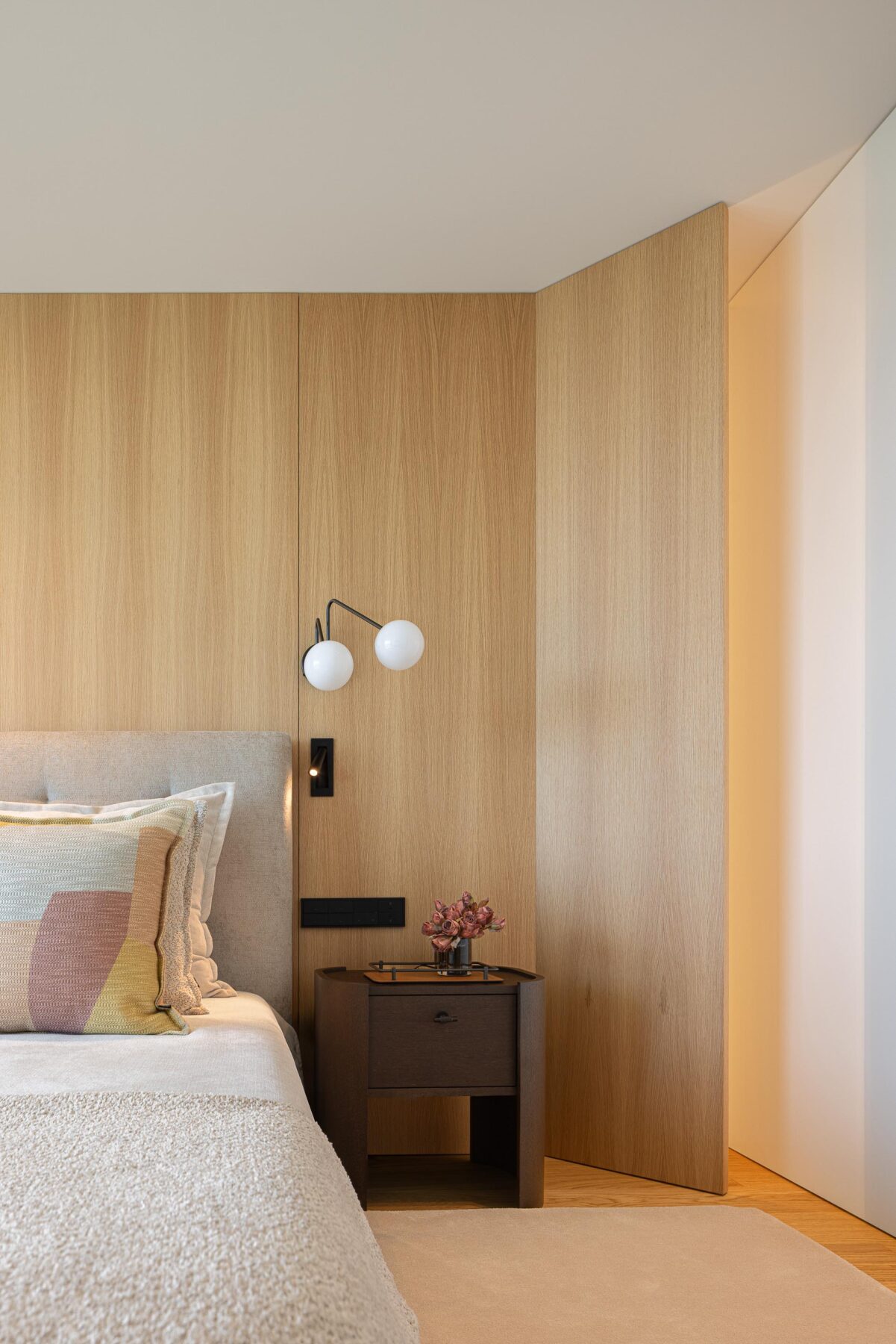 Quarto principal com parede de cabeceira em madeira mel, candeeiro de parede e mesa de cabeceira escura — Casa FJ arquitectura MIL870 + GRAUON fotografia Ivo Tavares