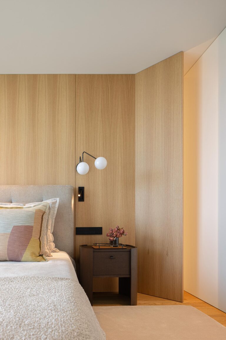 Quarto principal com parede de cabeceira em madeira mel, candeeiro de parede e mesa de cabeceira escura — Casa FJ arquitectura MIL870 + GRAUON fotografia Ivo Tavares