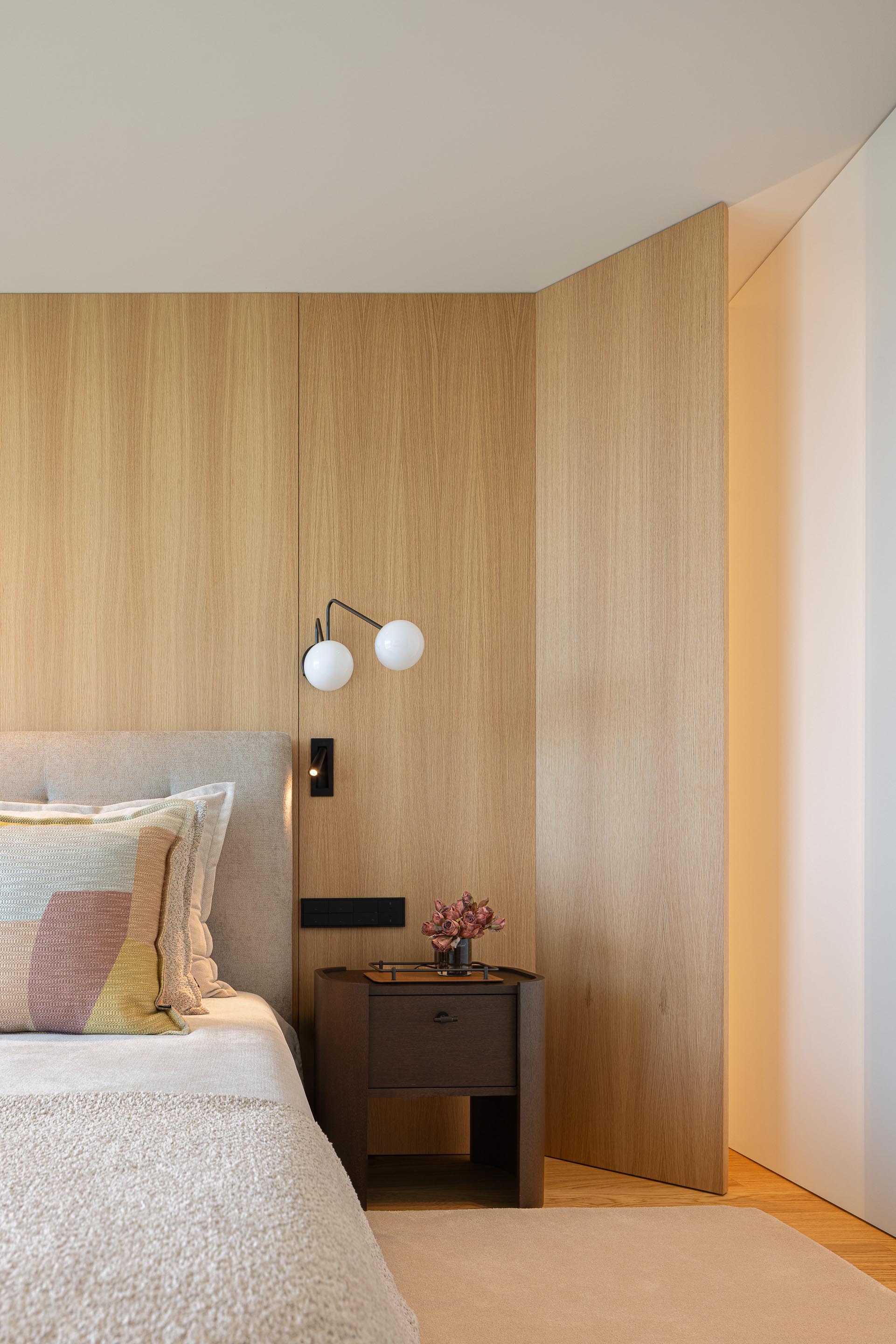 Quarto principal com parede de cabeceira em madeira mel, candeeiro de parede e mesa de cabeceira escura — Casa FJ arquitectura MIL870 + GRAUON fotografia Ivo Tavares