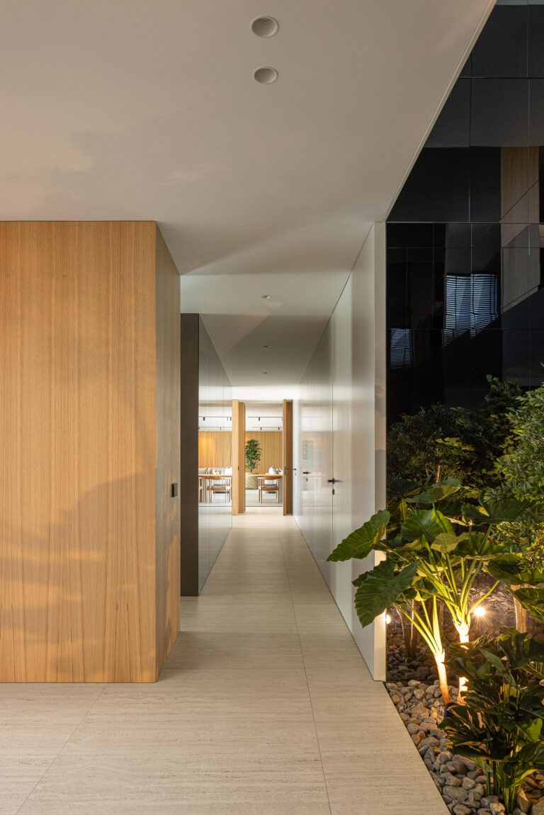 Corredor do rés do chão com pavimento em pedra clara, paredes brancas e jardim exterior iluminado — Casa FJ arquitectura MIL870 + GRAUON fotografia Ivo Tavares