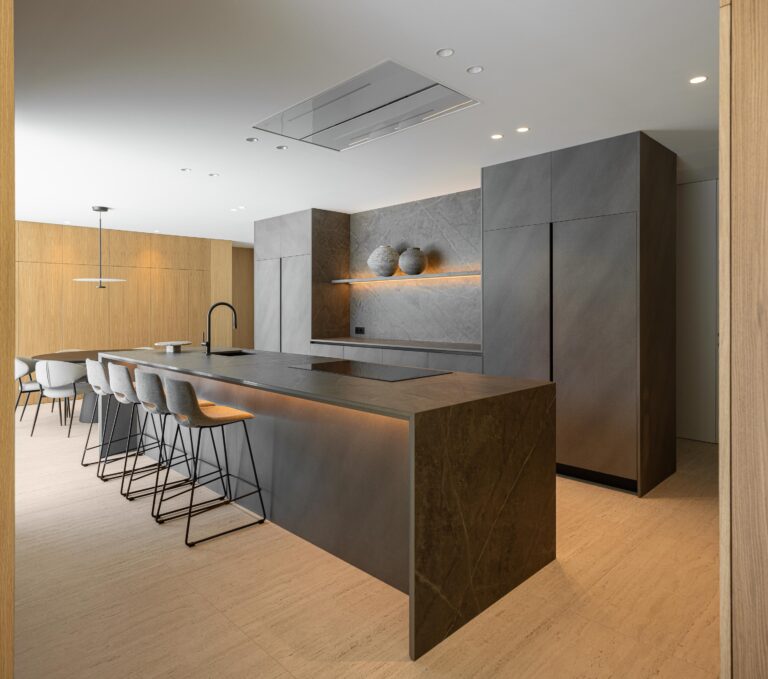 Cozinha com ilha e armários em pedra escura, pavimento em pedra clara e iluminação integrada — Casa FJ arquitectura MIL870 + GRAUON fotografia Ivo Tavares
