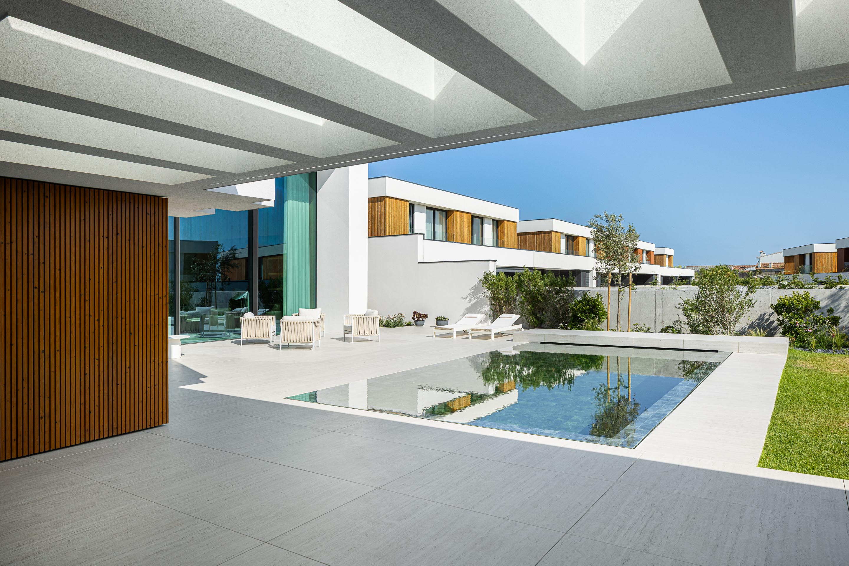 Zona da piscina com piscina retangular, pavimento em pedra clara e pérgola com estrutura branca — Casa FJ arquitectura MIL870 + GRAUON fotografia Ivo Tavares