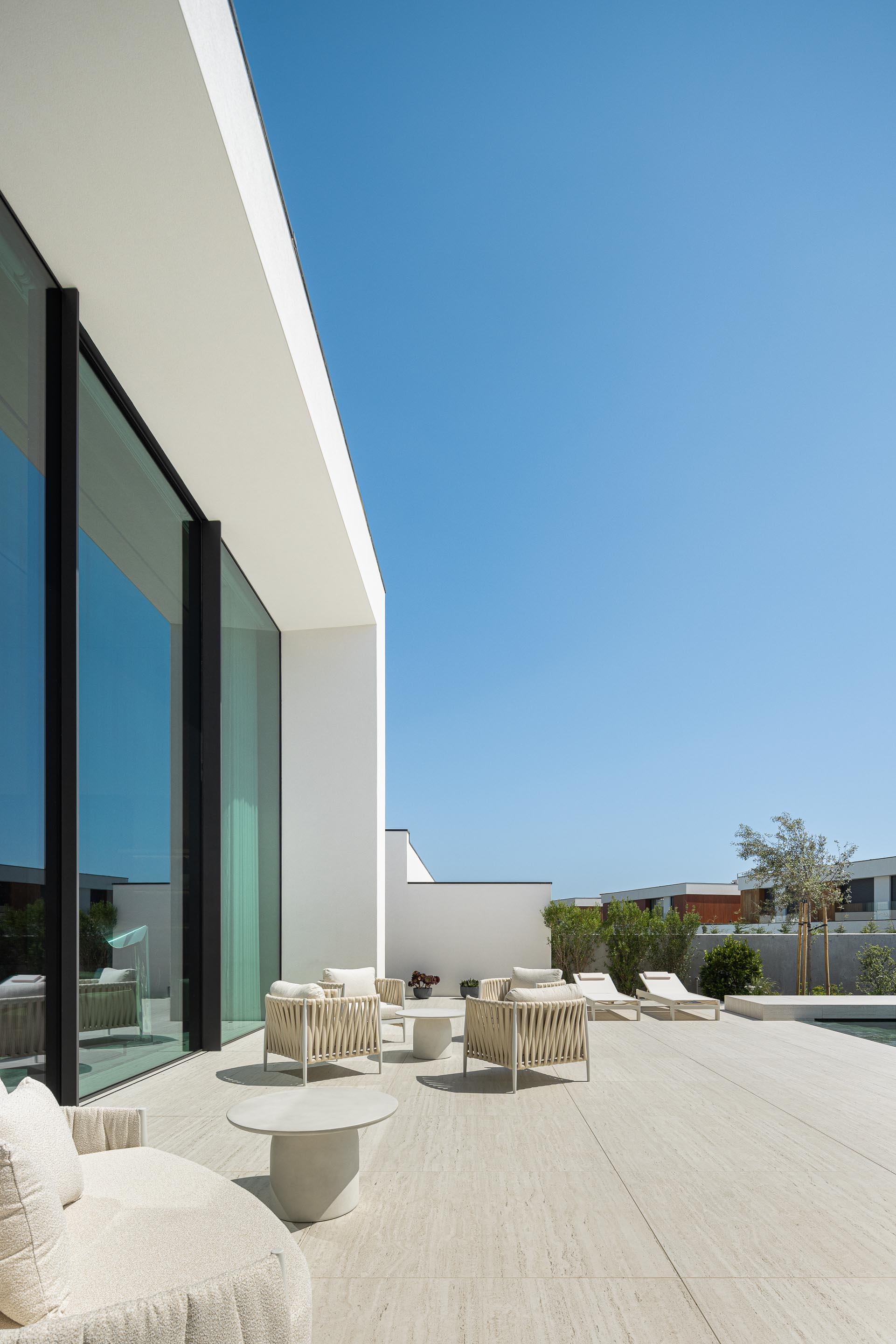 Terraço exterior com pavimento em pedra clara, mobiliário branco e grandes vãos envidraçados — Casa FJ arquitectura MIL870 + GRAUON fotografia Ivo Tavares