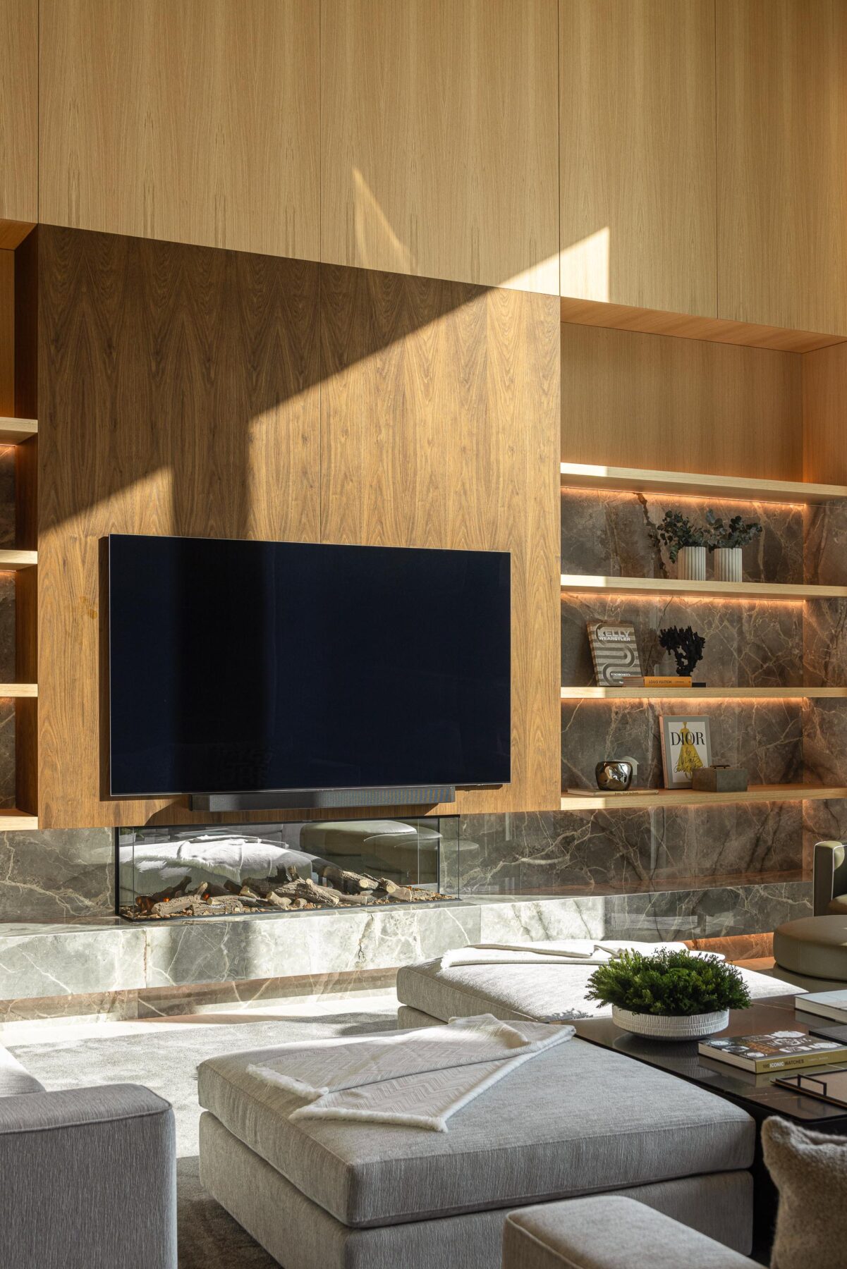 Sala de estar com lareira e TV, prateleiras iluminadas em mármore e revestimento em madeira escura — Casa FJ arquitectura MIL870 + GRAUON fotografia Ivo Tavares