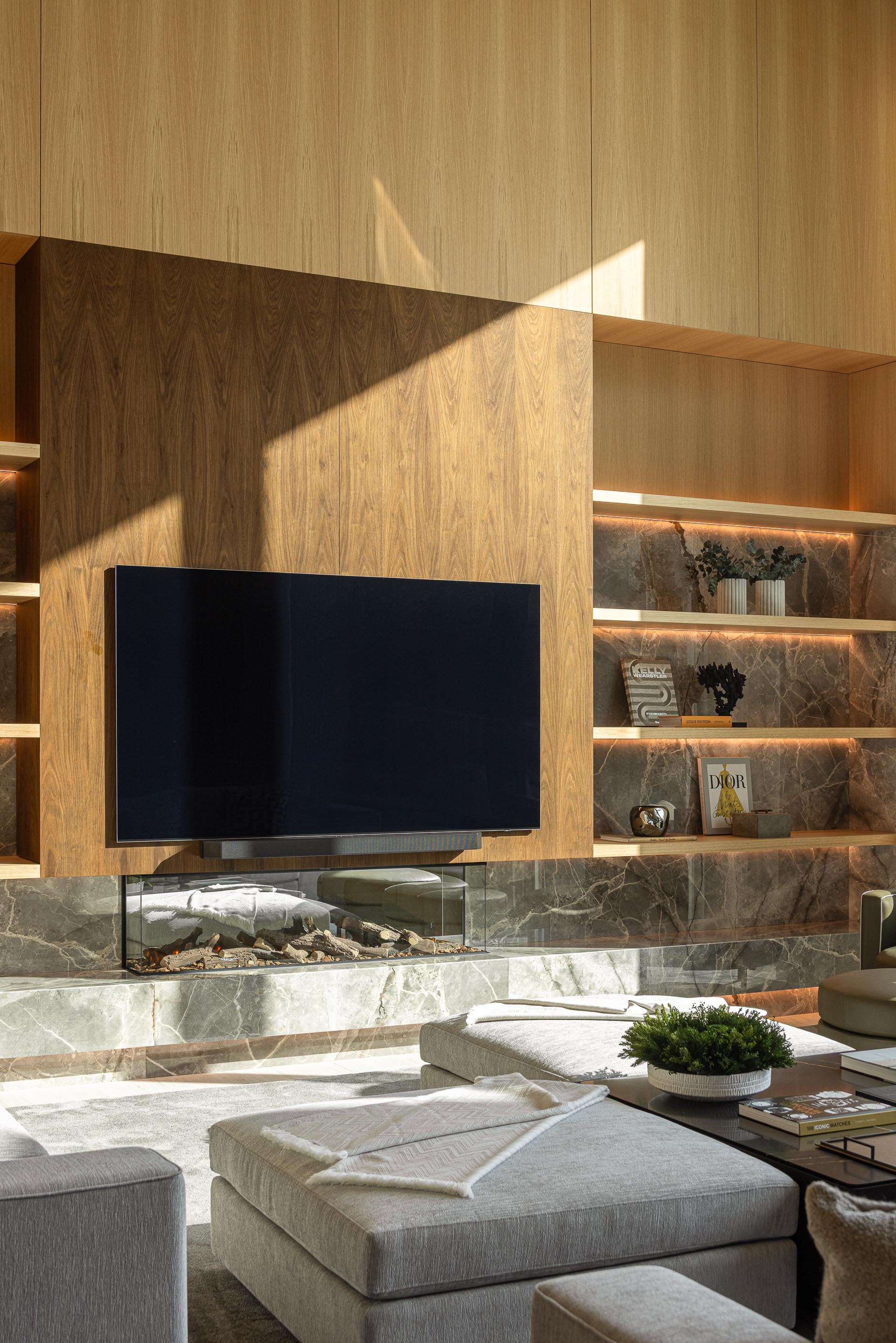 Sala de estar com lareira e TV, prateleiras iluminadas em mármore e revestimento em madeira escura — Casa FJ arquitectura MIL870 + GRAUON fotografia Ivo Tavares
