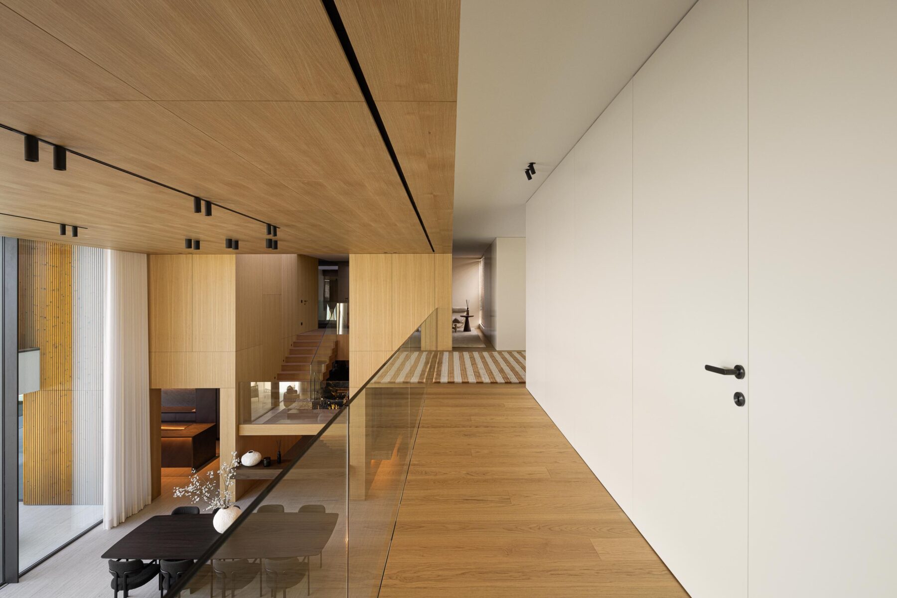 Corredor do pavimento superior com pavimento em madeira clara, guarda-corpos em vidro e vista para a sala — Casa FJ arquitectura MIL870 + GRAUON fotografia Ivo Tavares