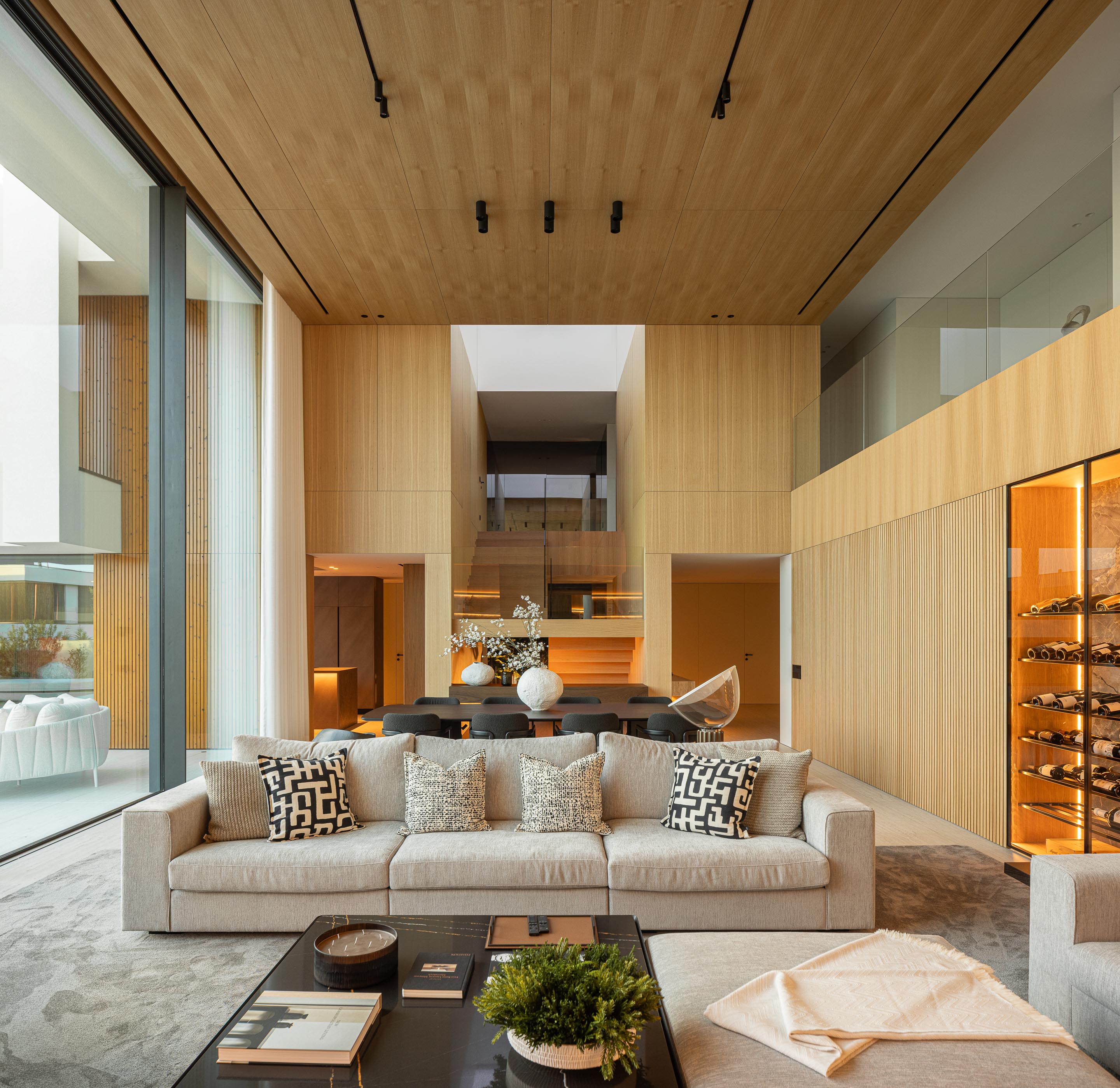 Sala de estar com pé-direito duplo, teto e paredes em madeira mel e garrafeira iluminada — Casa FJ arquitectura MIL870 + GRAUON fotografia Ivo Tavares