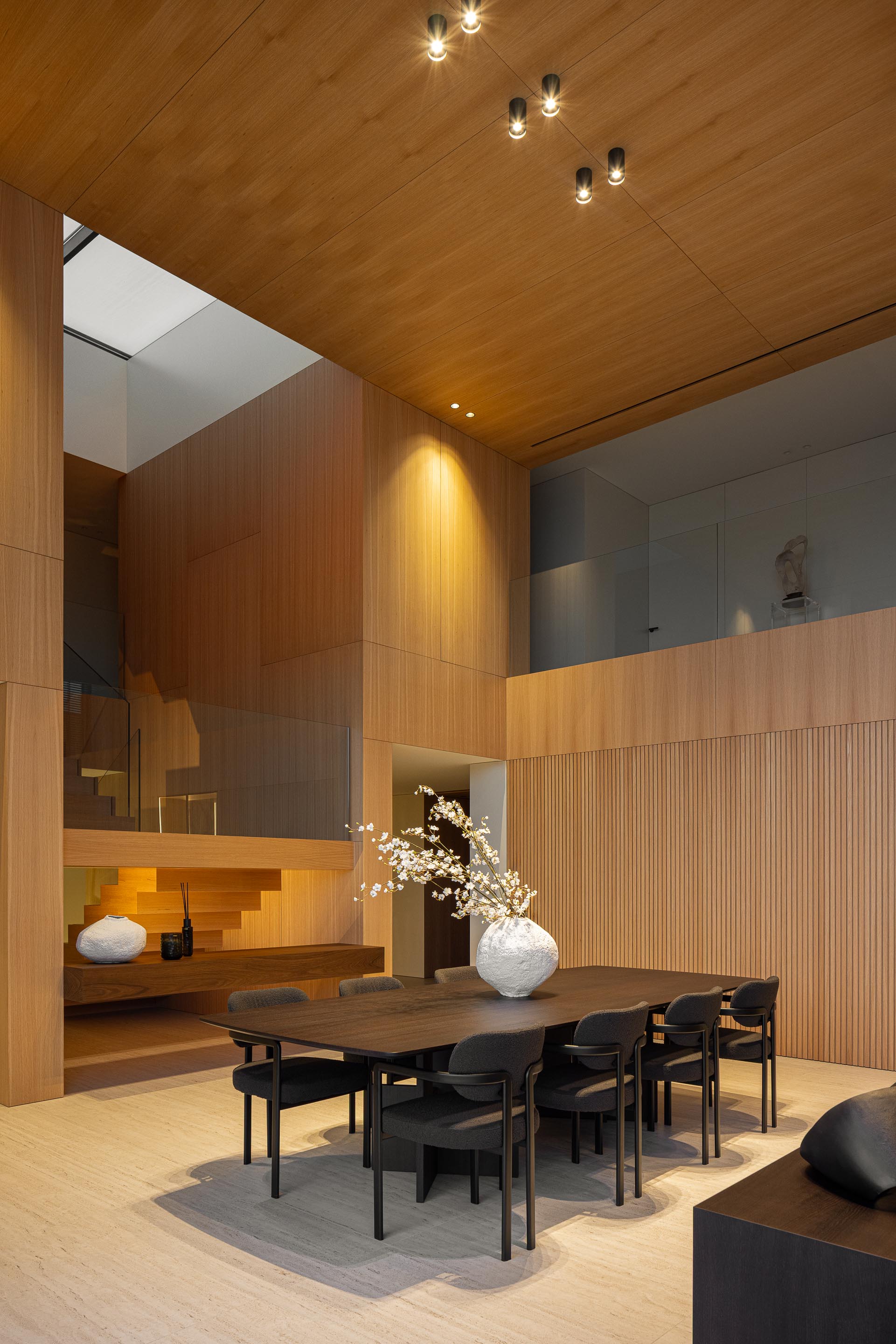 Sala de jantar com mesa escura, paredes em madeira mel e escadaria iluminada — Casa FJ arquitectura MIL870 + GRAUON fotografia Ivo Tavares
