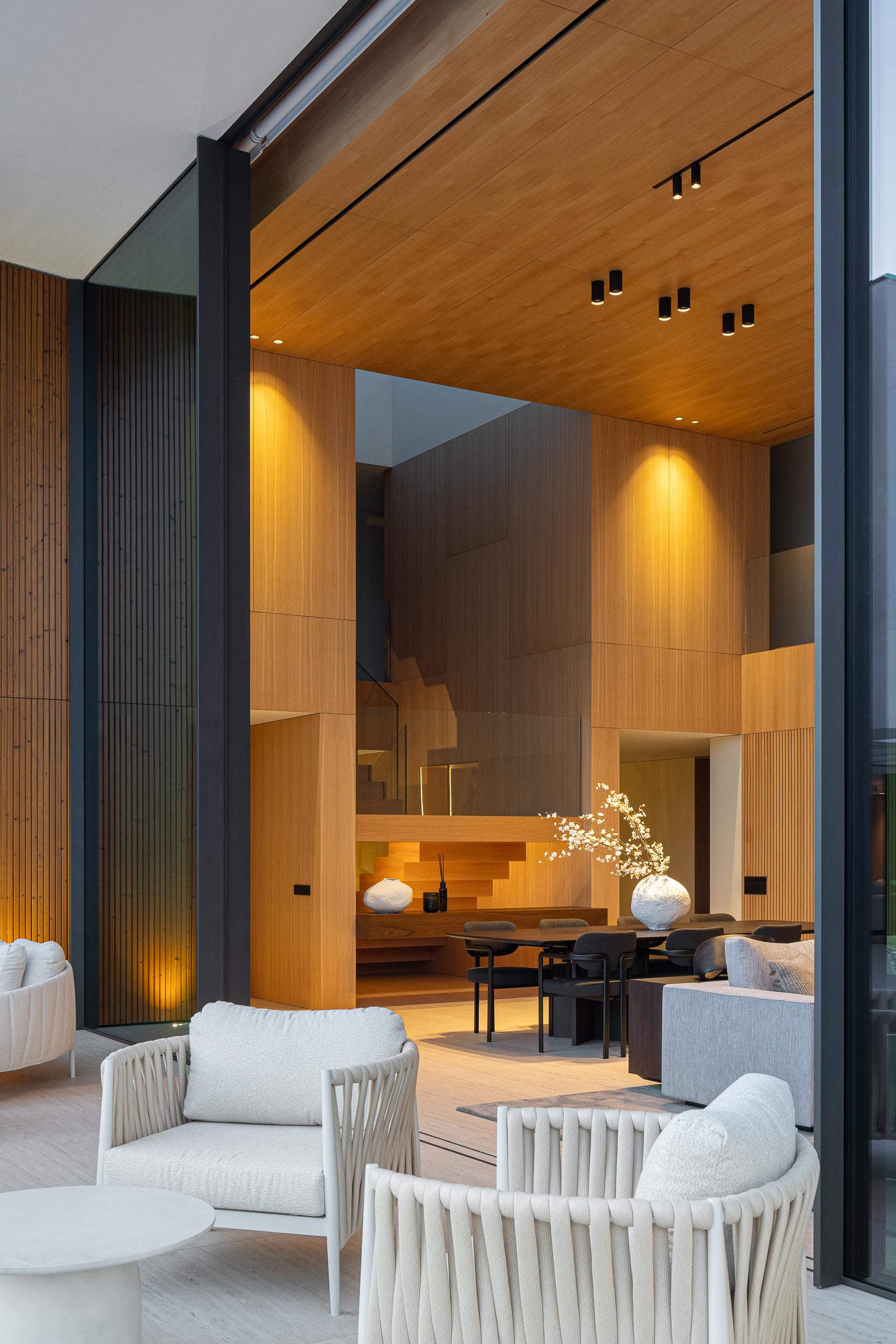 Sala de estar com grandes vãos envidraçados, mobiliário de exterior e piscina iluminada — Casa FJ arquitectura MIL870 + GRAUON fotografia Ivo Tavares