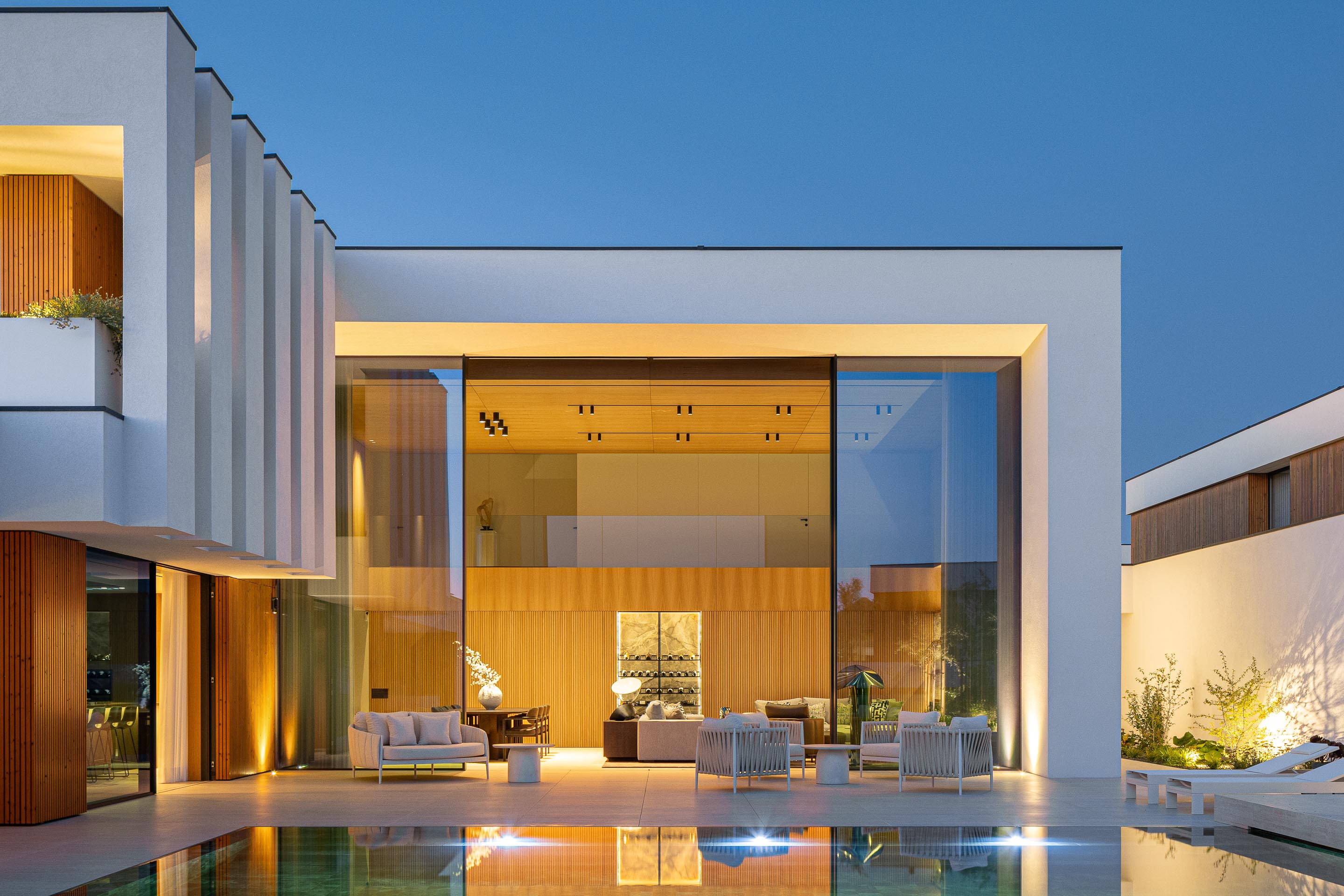 Fachada posterior com volumes brancos, revestimento em madeira mel e piscina iluminada — Casa FJ arquitectura MIL870 + GRAUON fotografia Ivo Tavares
