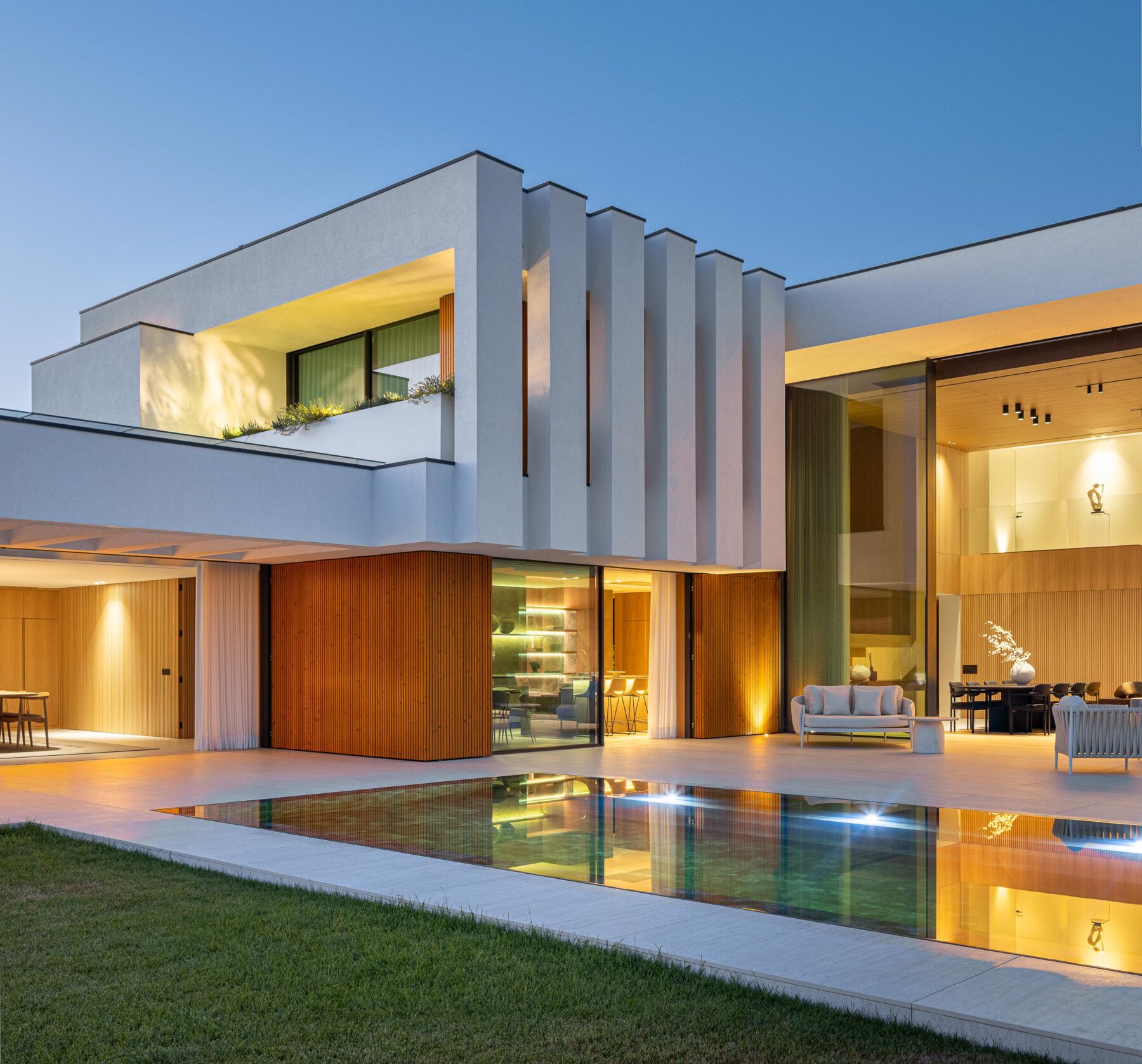 Fachada posterior com volumes brancos, revestimento em madeira mel e piscina retangular iluminada — Casa FJ arquitectura MIL870 + GRAUON fotografia Ivo Tavares