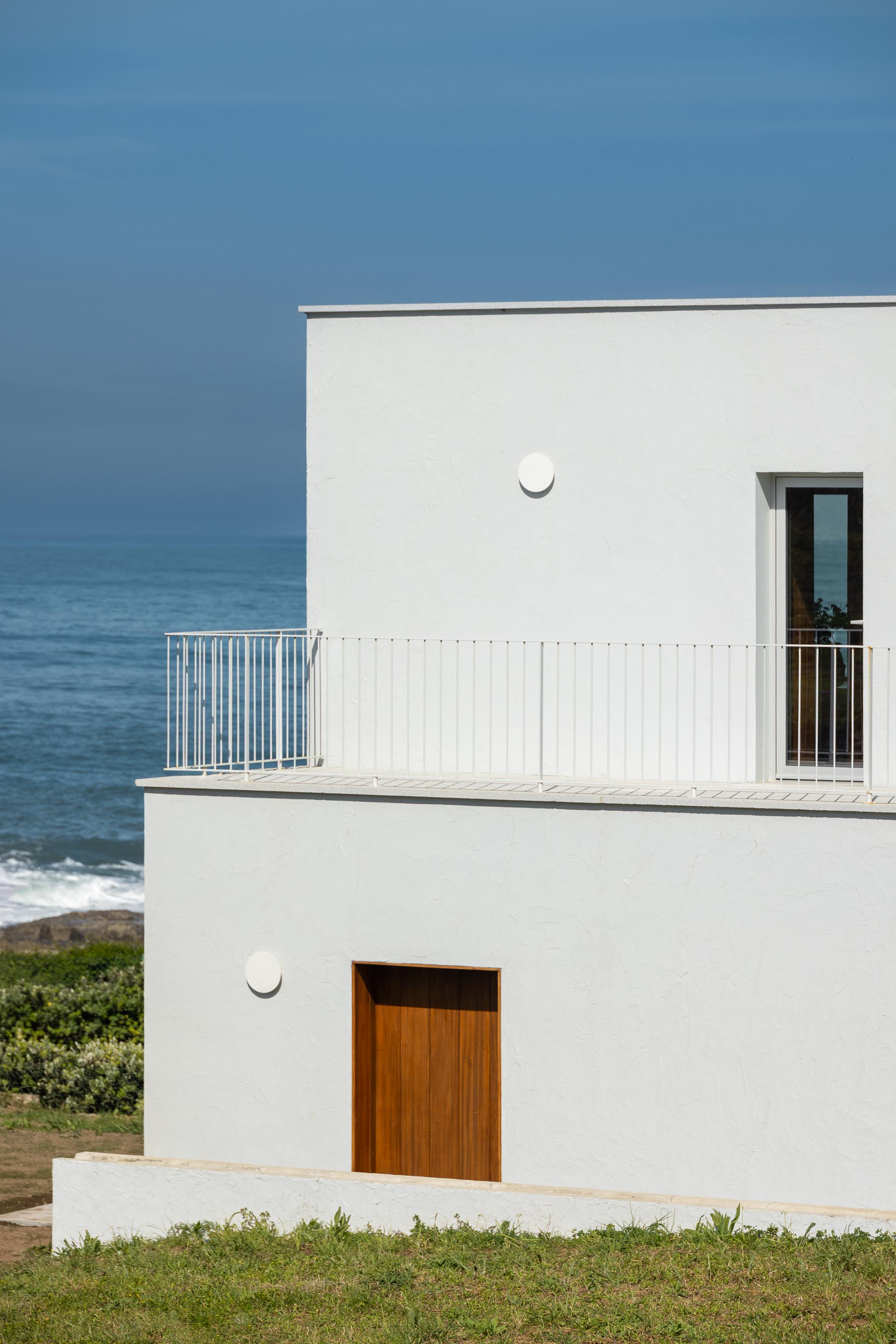 Fachada branca texturada com varanda e porta de madeira mel, em frente ao oceano — CASA ÂNCORA arquitectura Tiago Sousa Arquitecto fotografia Ivo Tavares
