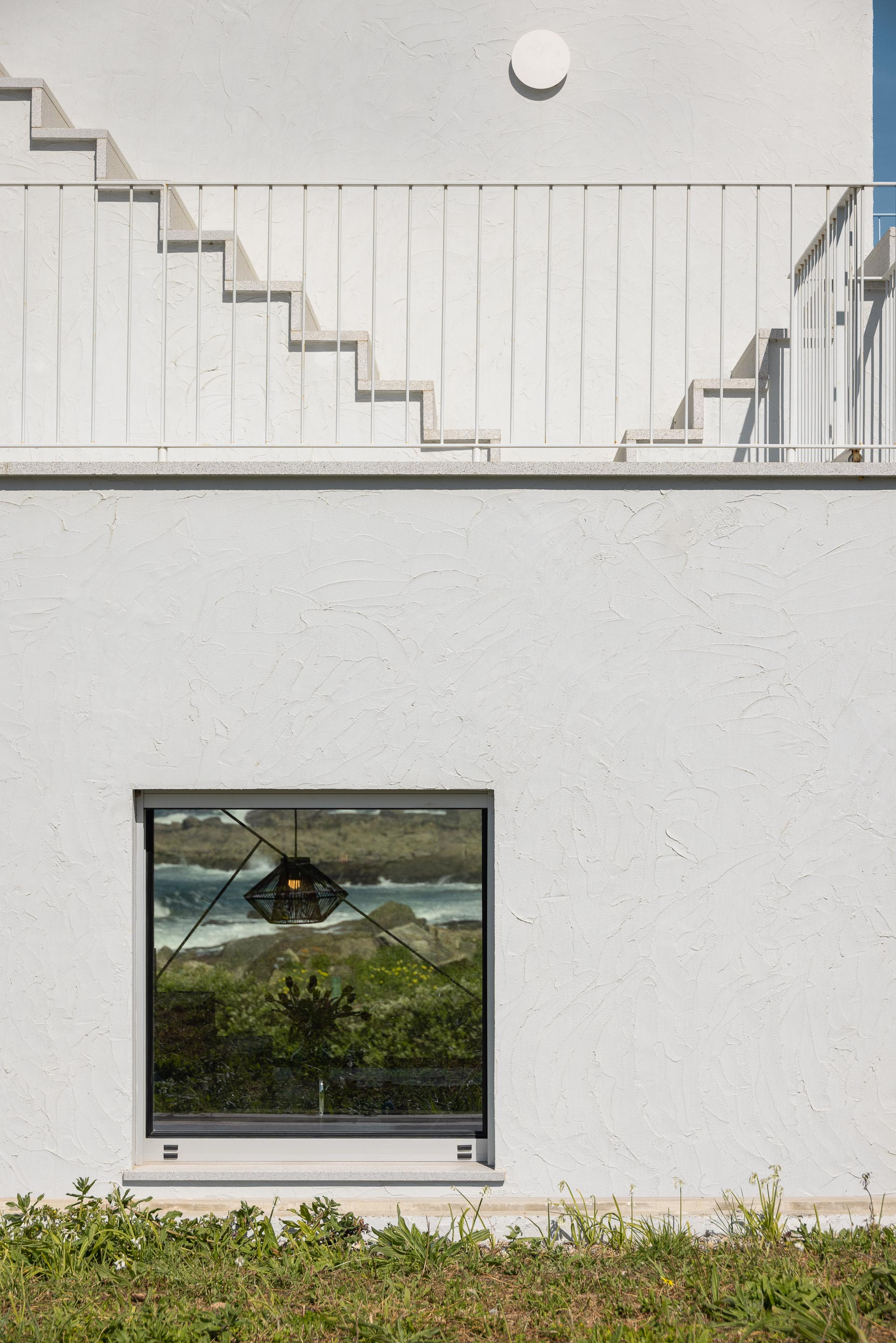 Fachada branca texturada com vão quadrado e reflexo do mar, com escadaria exterior visível — CASA ÂNCORA arquitectura Tiago Sousa Arquitecto fotografia Ivo Tavares