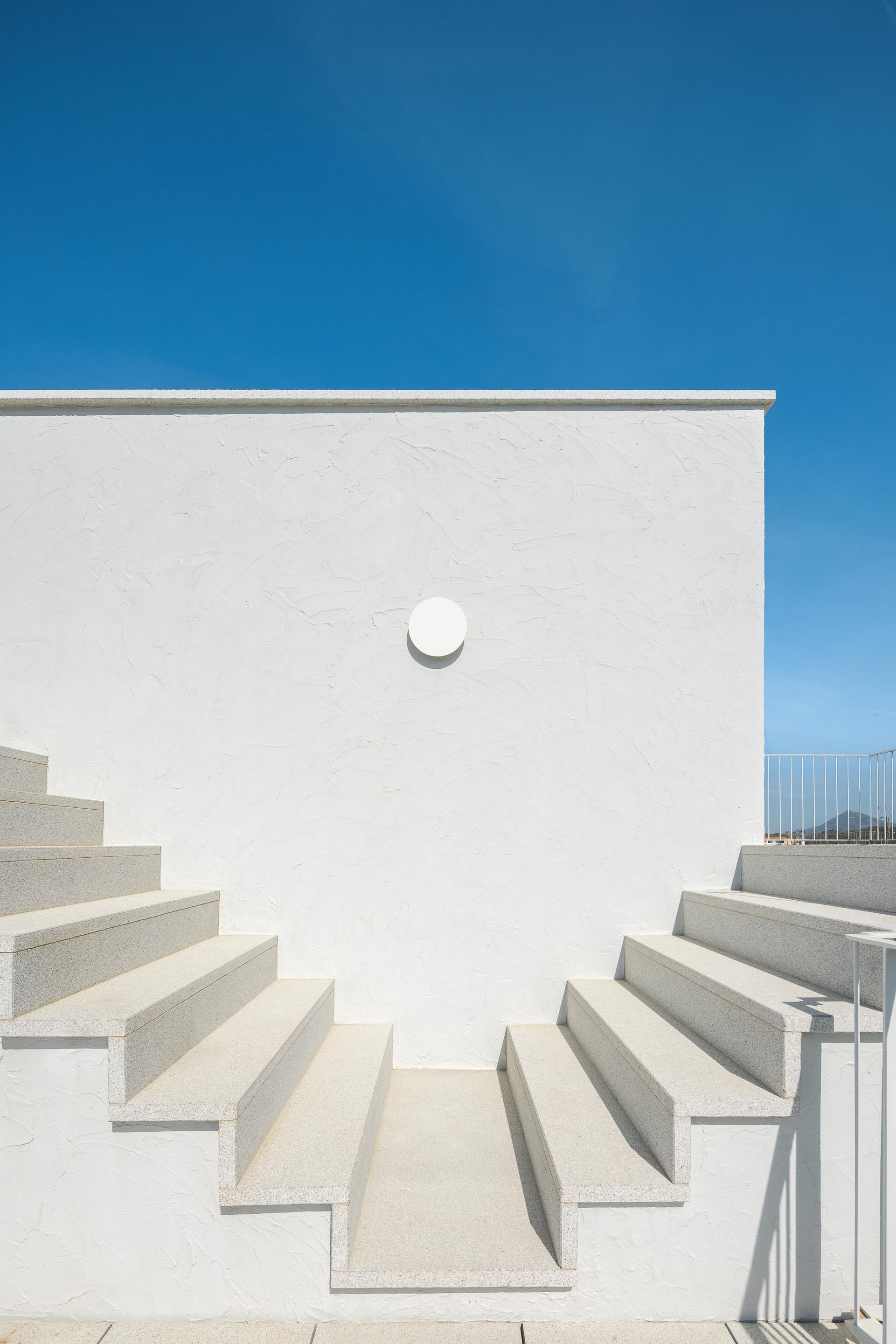 Escadaria exterior em pedra clara sobre fachada branca texturada, com candeeiro circular — CASA ÂNCORA arquitectura Tiago Sousa Arquitecto fotografia Ivo Tavares