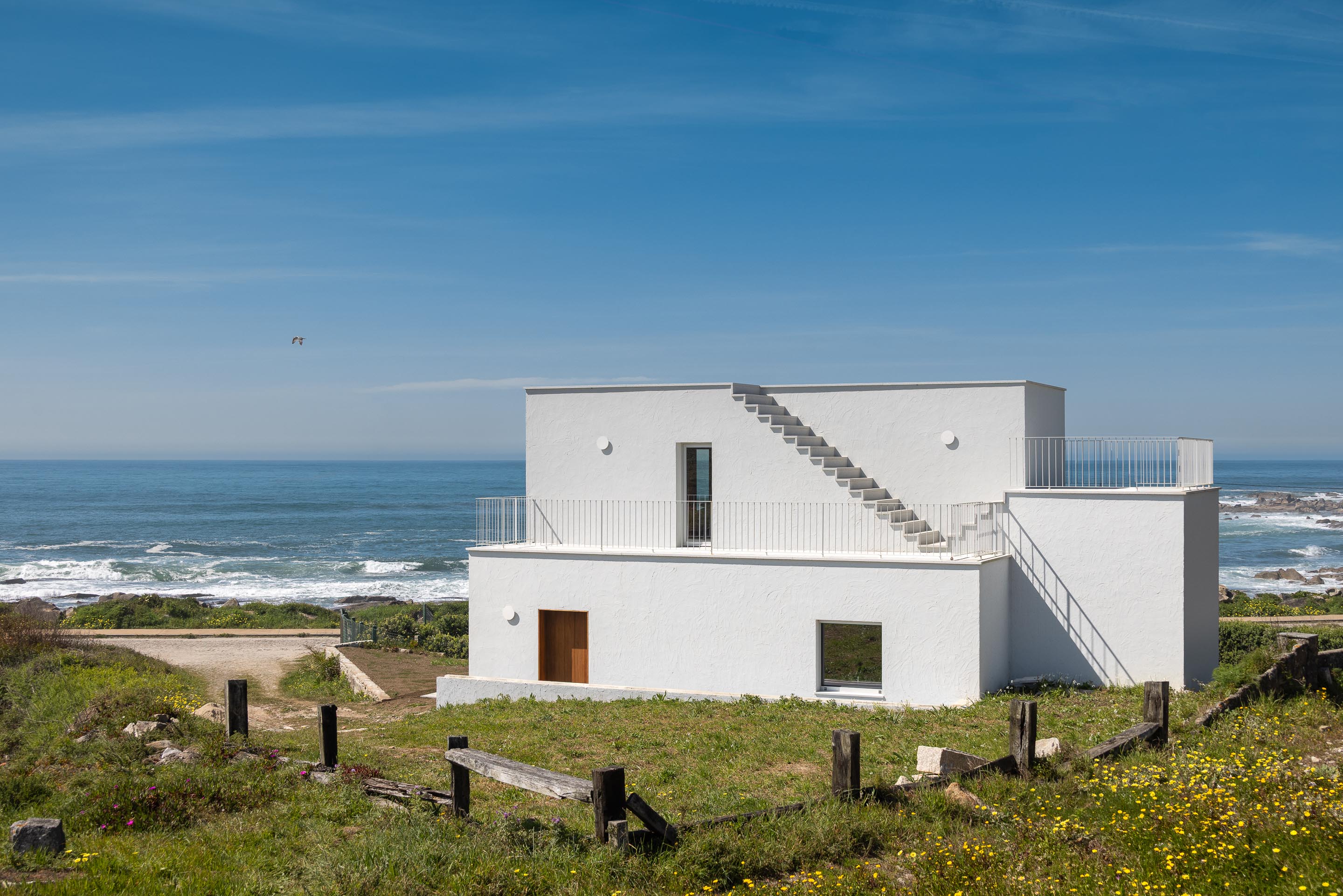 Moradia branca de volumes compactos e escadarias exteriores, inserida na paisagem costeira — CASA ÂNCORA arquitectura Tiago Sousa Arquitecto fotografia Ivo Tavares