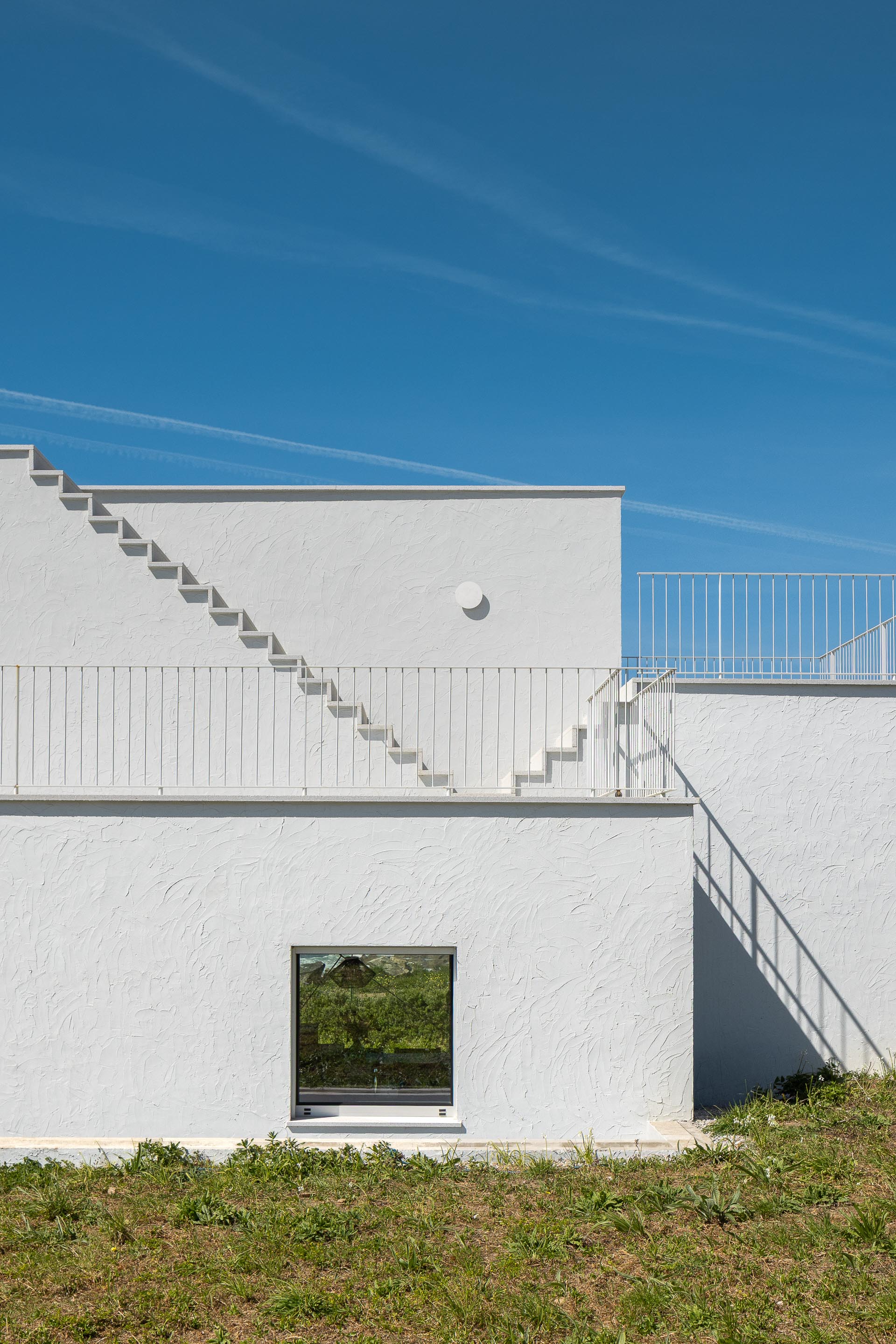 Fachada branca texturada com vão quadrado e escadaria exterior, sob luz solar intensa — CASA ÂNCORA arquitectura Tiago Sousa Arquitecto fotografia Ivo Tavares
