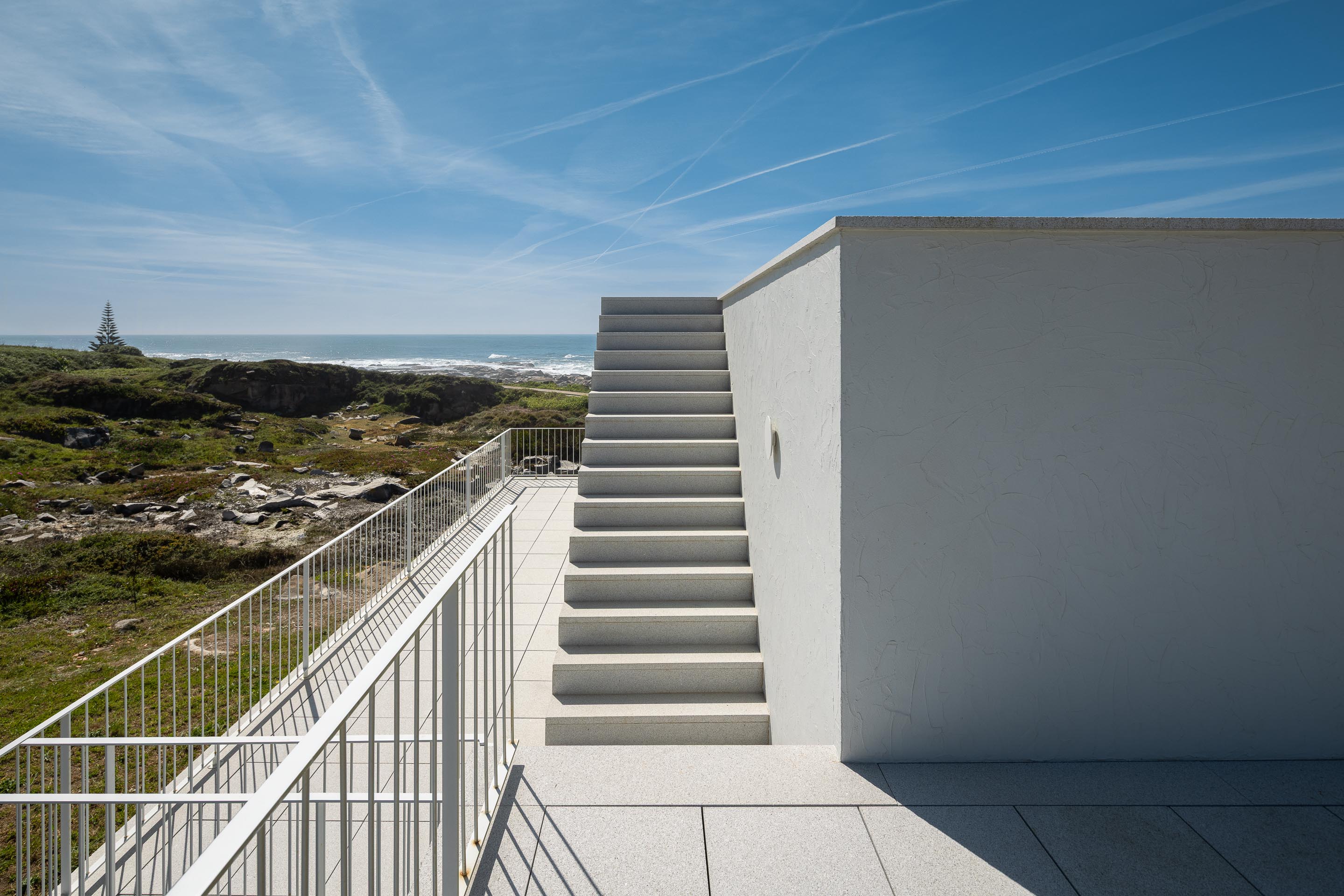 Varanda e escadaria exterior em pedra clara, com guarda-corpos metálicos brancos e vista para o mar — CASA ÂNCORA arquitectura Tiago Sousa Arquitecto fotografia Ivo Tavares