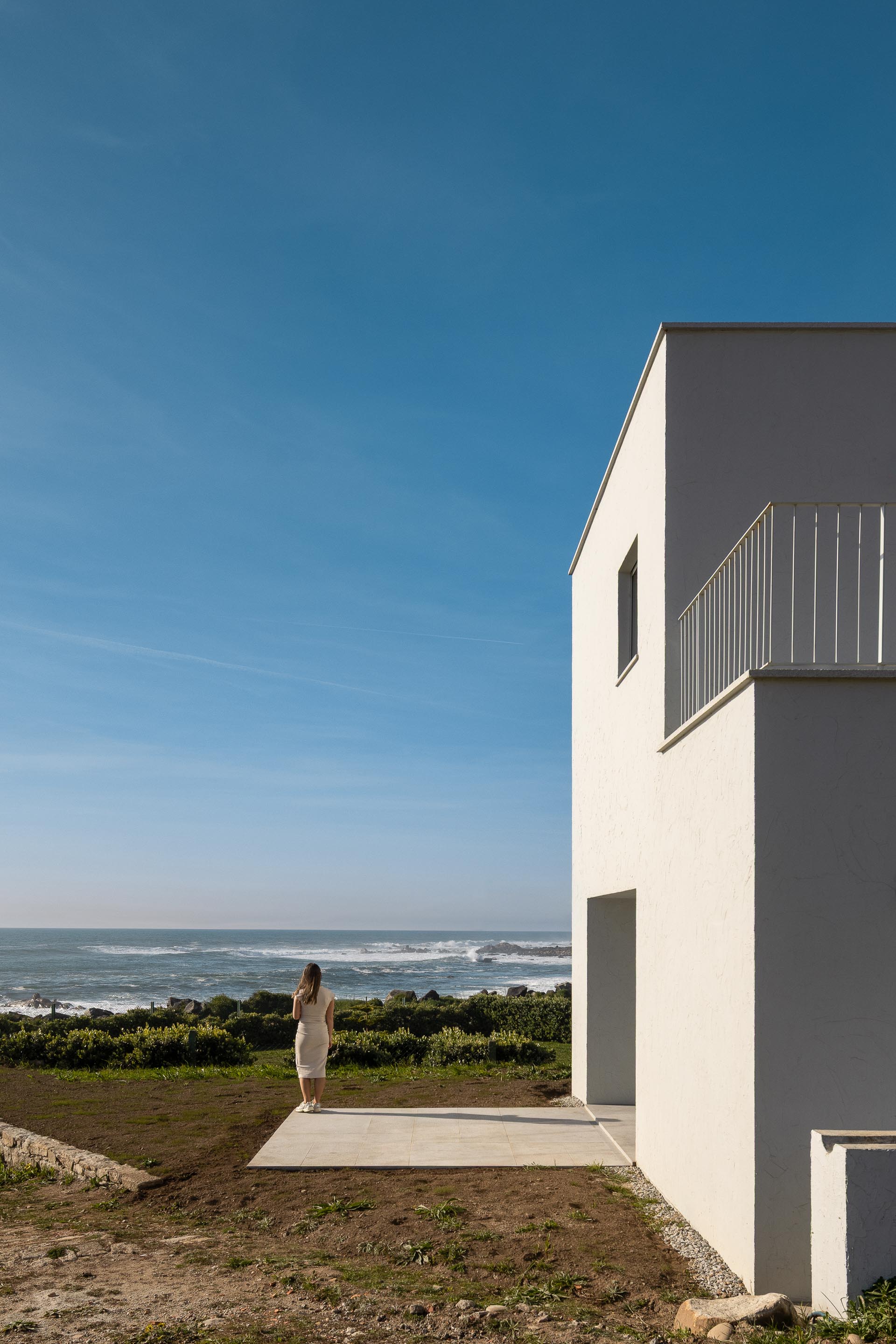 Terraço exterior com pavimento claro, adjacente à moradia branca, com vista para o mar — CASA ÂNCORA arquitectura Tiago Sousa Arquitecto fotografia Ivo Tavares