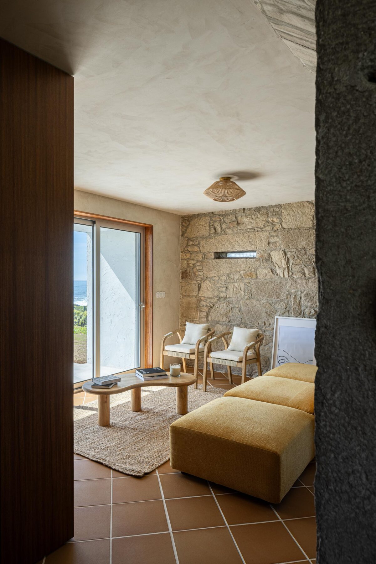 Sala de estar com pavimento cerâmico de barro e parede de pedra, mobiliário em madeira e estofado amarelo — CASA ÂNCORA arquitectura Tiago Sousa Arquitecto fotografia Ivo Tavares