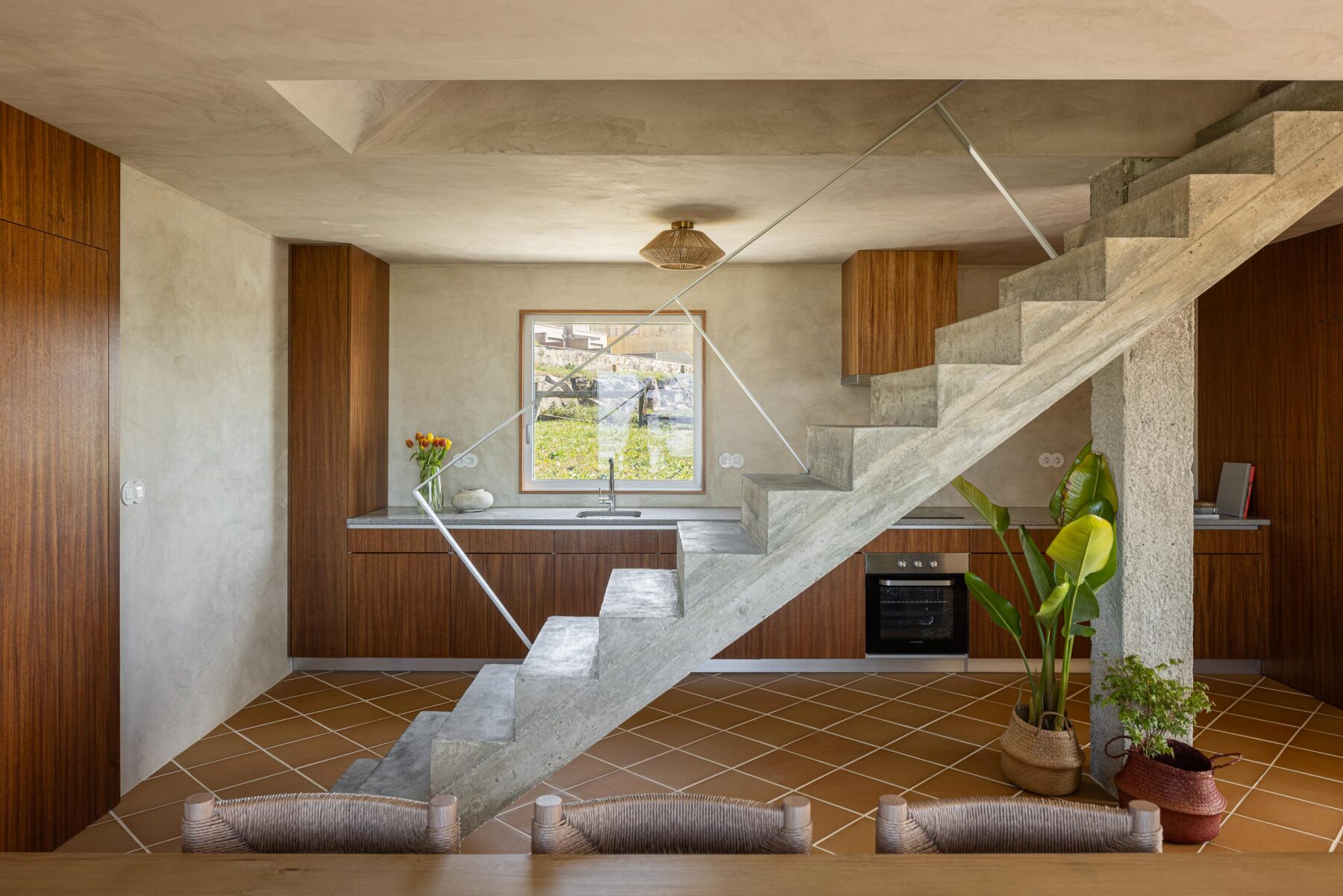 Cozinha e sala de jantar com pavimento cerâmico de barro, escadaria em betão aparente e armários de madeira — CASA ÂNCORA arquitectura Tiago Sousa Arquitecto fotografia Ivo Tavares