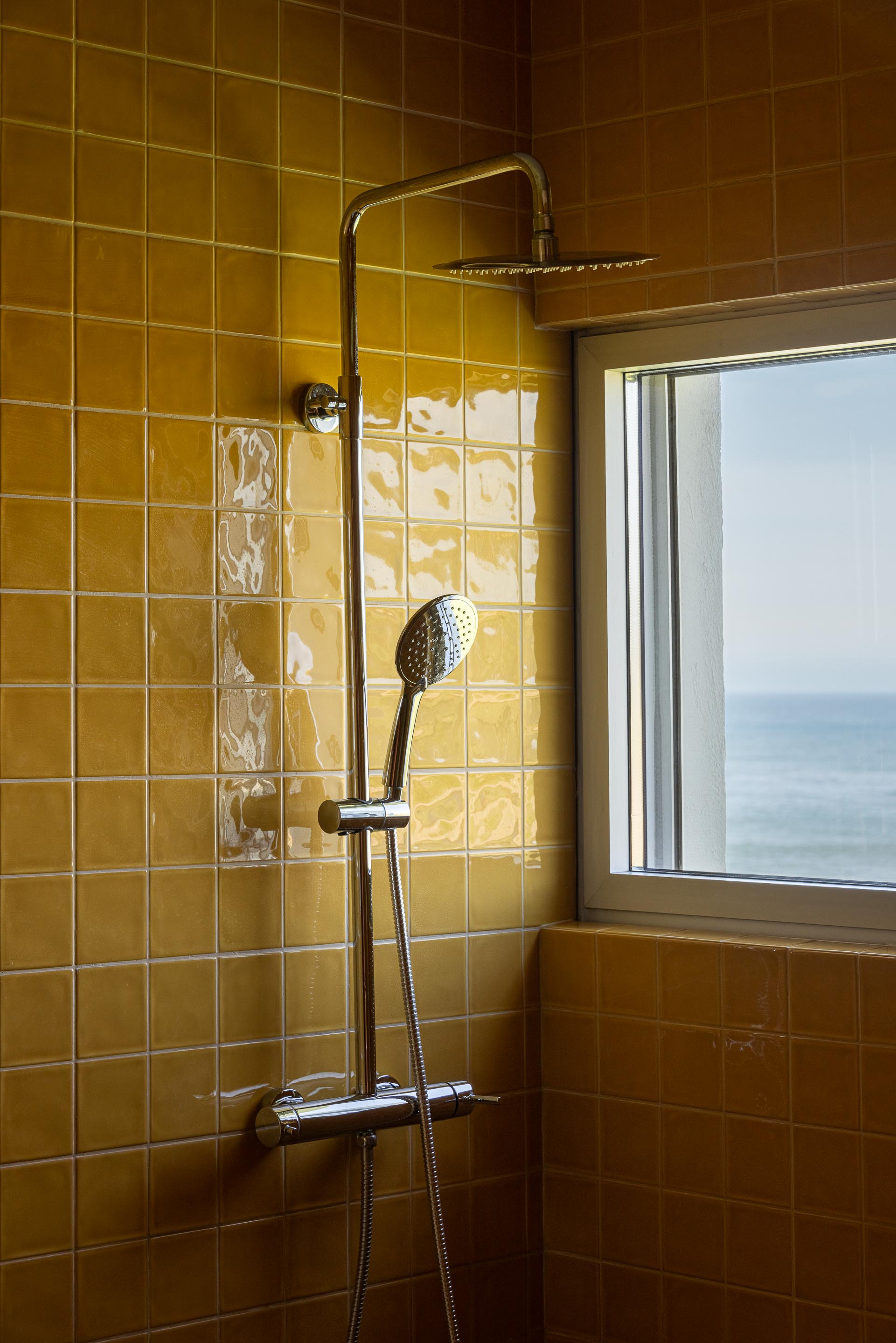 Casa de banho com revestimento em azulejo amarelo brilhante e chuveiro metálico, com vista para o mar — CASA ÂNCORA arquitectura Tiago Sousa Arquitecto fotografia Ivo Tavares