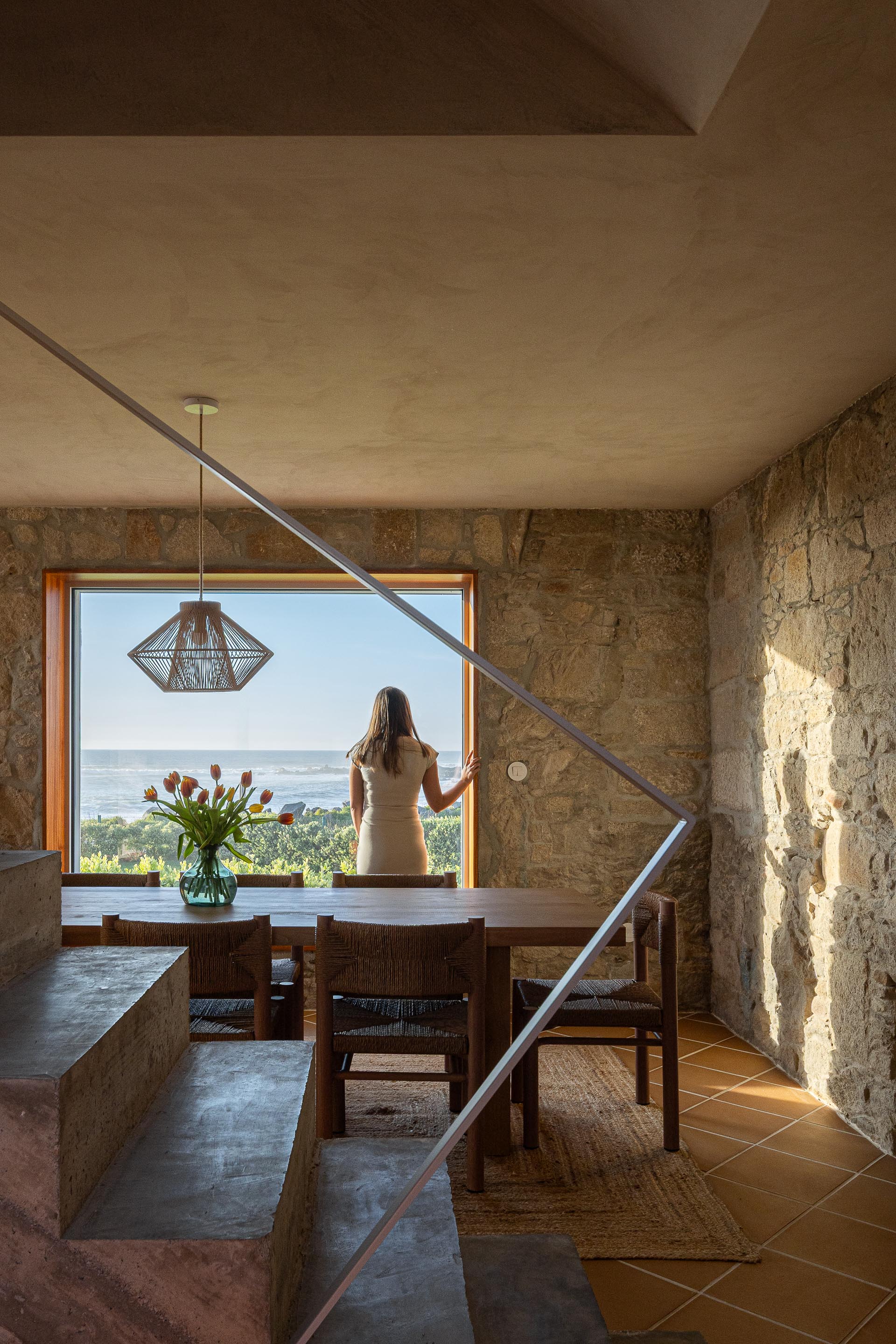 Sala de jantar com parede de pedra, pavimento cerâmico de barro e escadaria em betão aparente — CASA ÂNCORA arquitectura Tiago Sousa Arquitecto fotografia Ivo Tavares