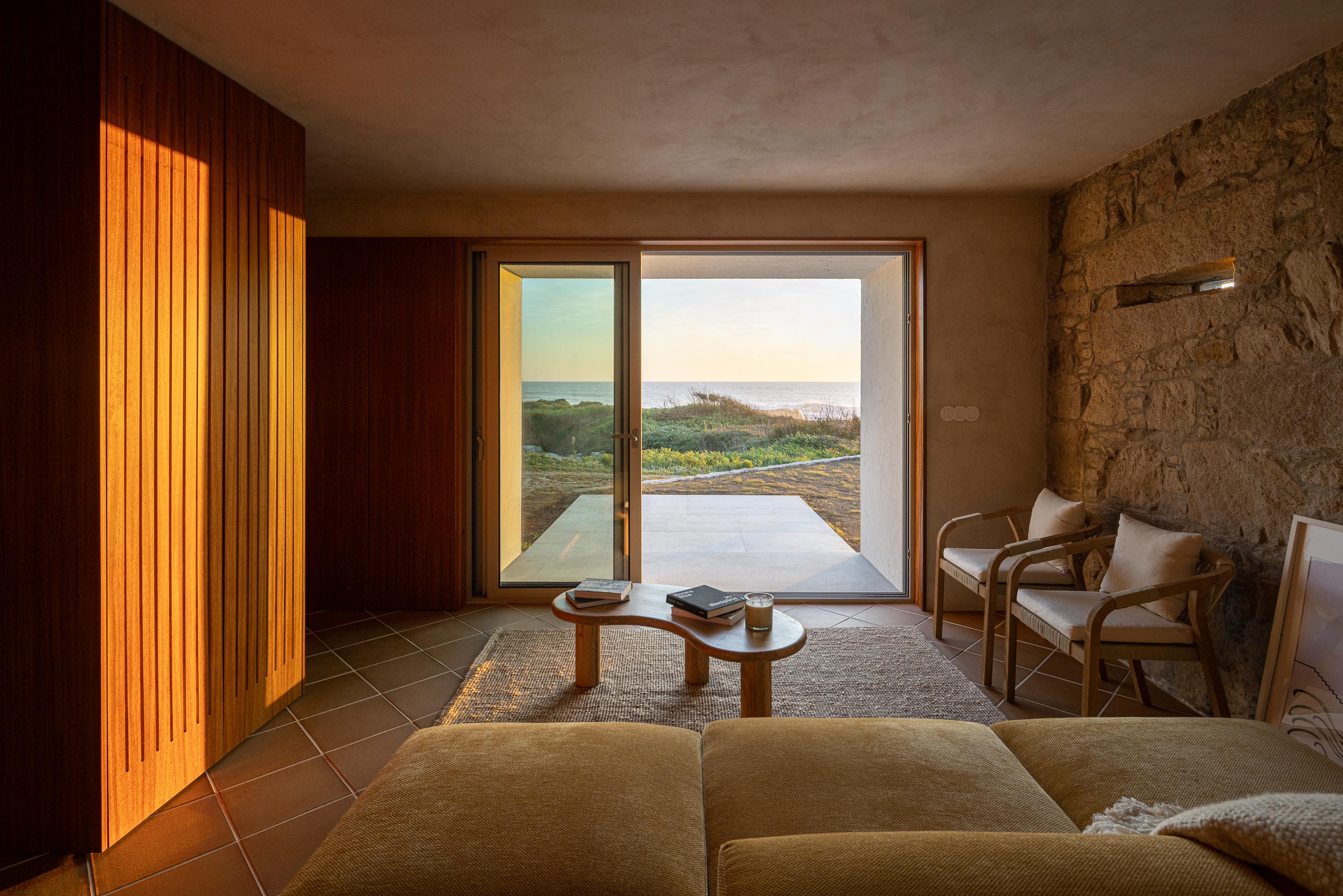 Sala de estar com pavimento cerâmico de barro, parede de pedra e vão de correr para o exterior — CASA ÂNCORA arquitectura Tiago Sousa Arquitecto fotografia Ivo Tavares