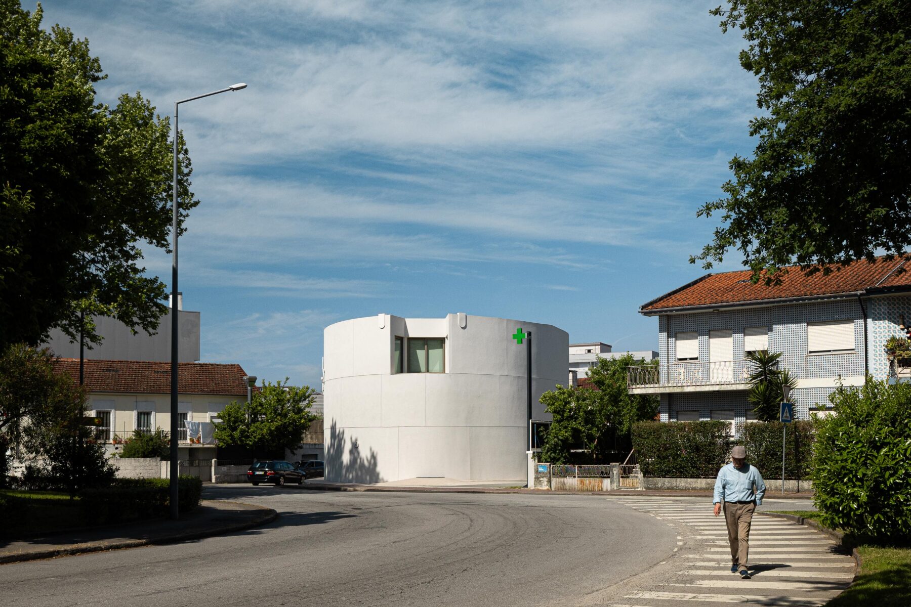 Fachada curva em EPS projetado branco, com vão de janela e sinalética verde, integrada no gaveto urbano — Farmácia São João arquitectura Tsou Arquitectos fotografia Ivo Tavares
