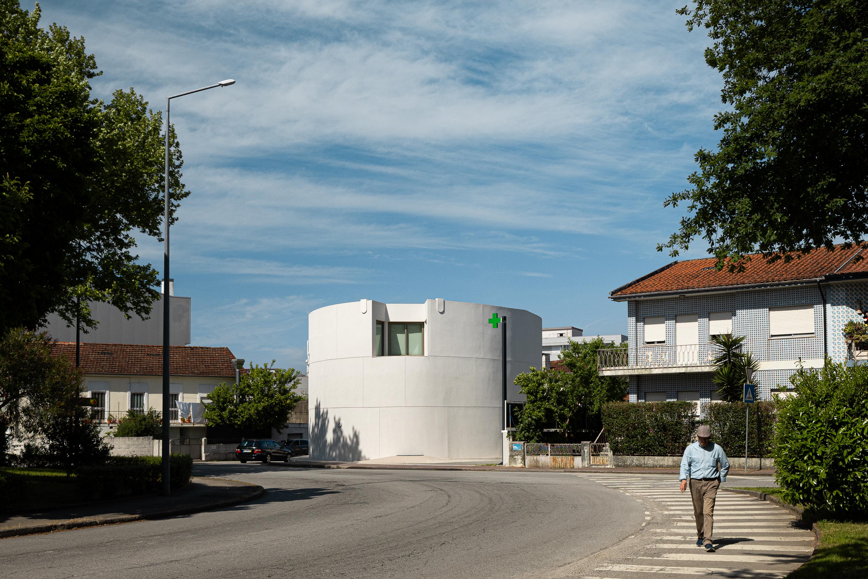 Fachada curva em EPS projetado branco, com vão de janela e sinalética verde, integrada no gaveto urbano — Farmácia São João arquitectura Tsou Arquitectos fotografia Ivo Tavares