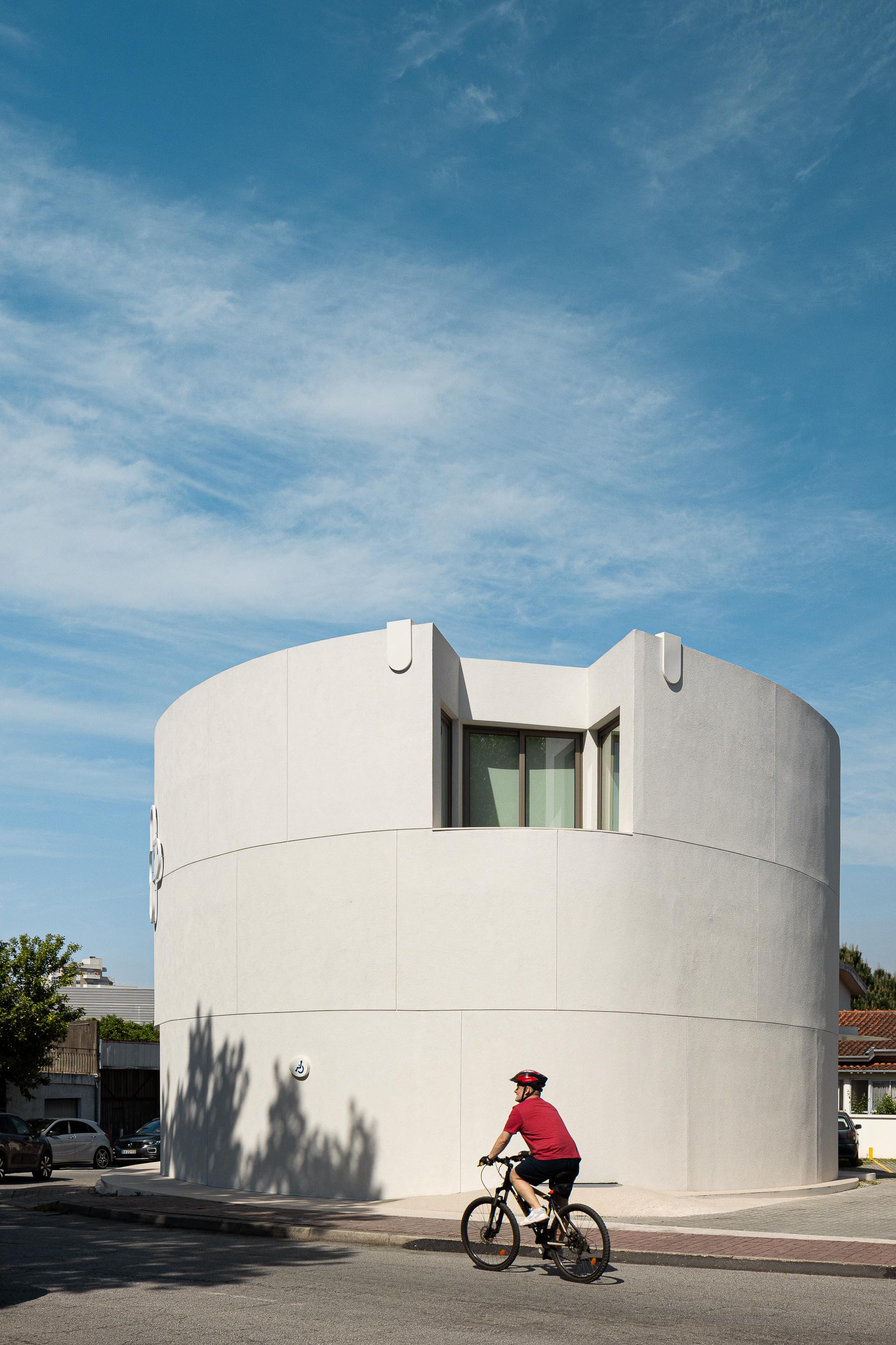 Fachada curva em EPS projetado branco com reentrância superior e vão de janela, sob céu azul — Farmácia São João arquitectura Tsou Arquitectos fotografia Ivo Tavares