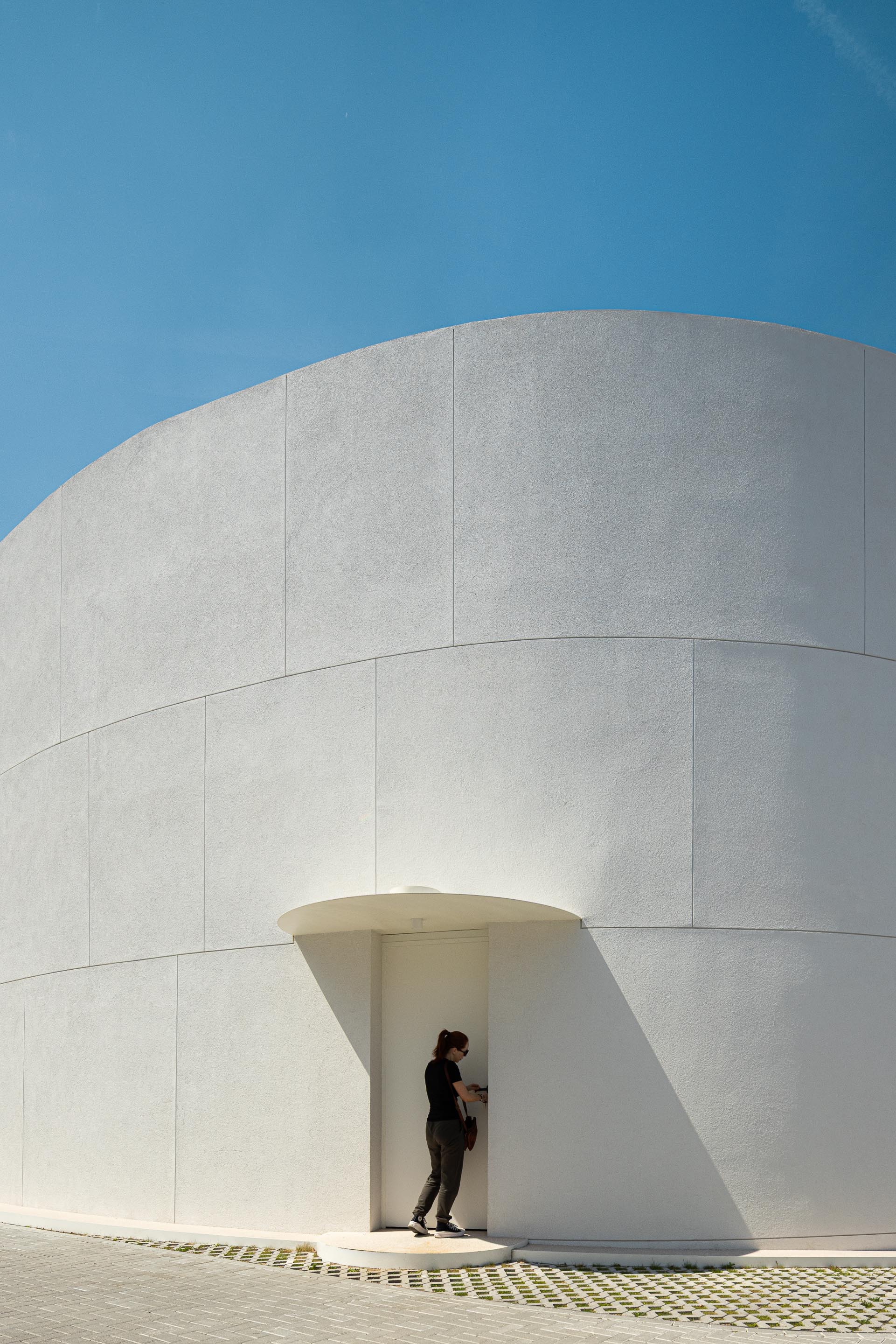 Entrada recuada na fachada curva em EPS projetado branco, com cobertura circular e pavimento em mármore de Estremoz — Farmácia São João arquitectura Tsou Arquitectos fotografia Ivo Tavares