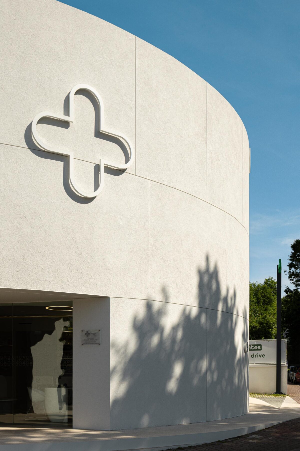Fachada curva em EPS projetado branco com sinalética em relevo e reclamo luminoso verde sobre jardim vertical — Farmácia São João arquitectura Tsou Arquitectos fotografia Ivo Tavares