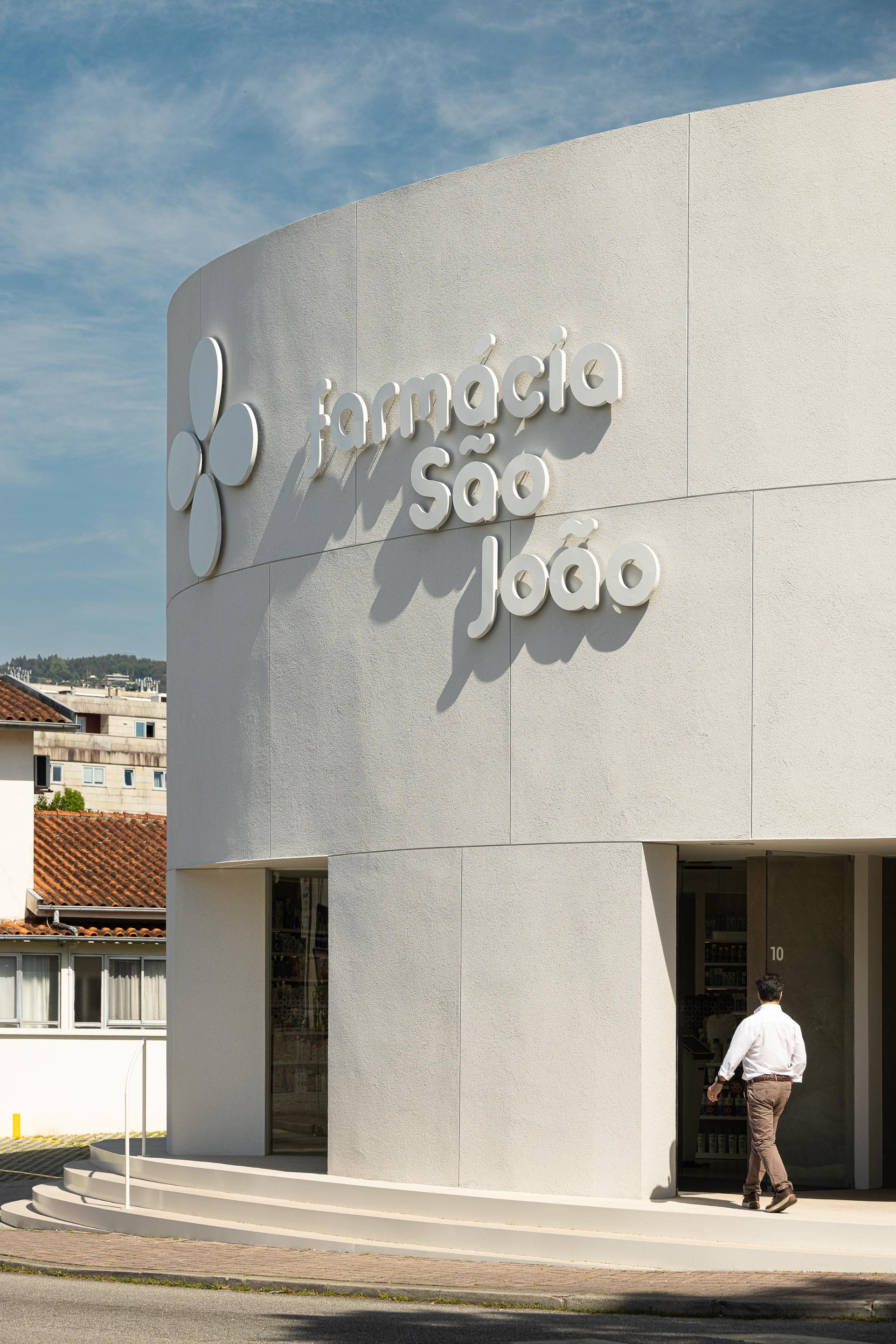 Fachada curva em EPS projetado branco com sinalética em relevo e entrada com degraus em mármore de Estremoz jateado — Farmácia São João arquitectura Tsou Arquitectos fotografia Ivo Tavares