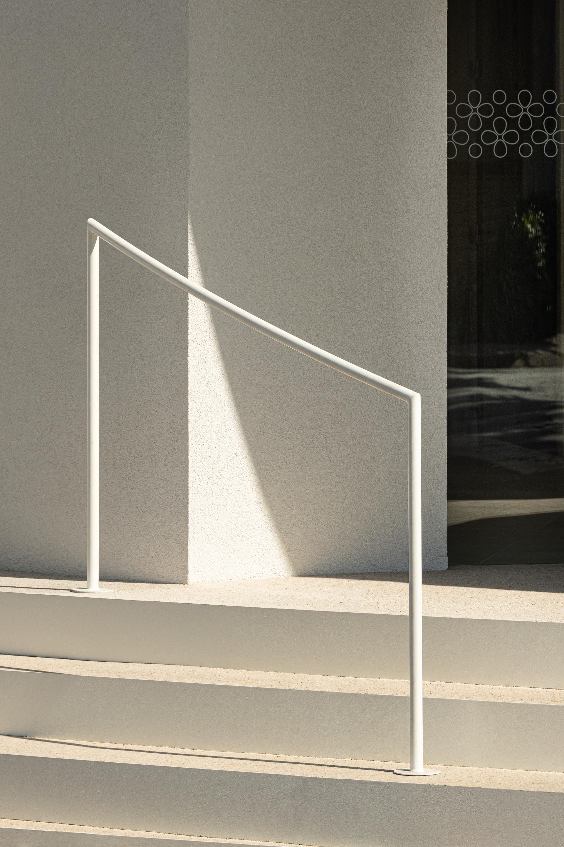 Degraus curvos em mármore de Estremoz jateado com corrimão metálico branco, junto à fachada em EPS projetado — Farmácia São João arquitectura Tsou Arquitectos fotografia Ivo Tavares