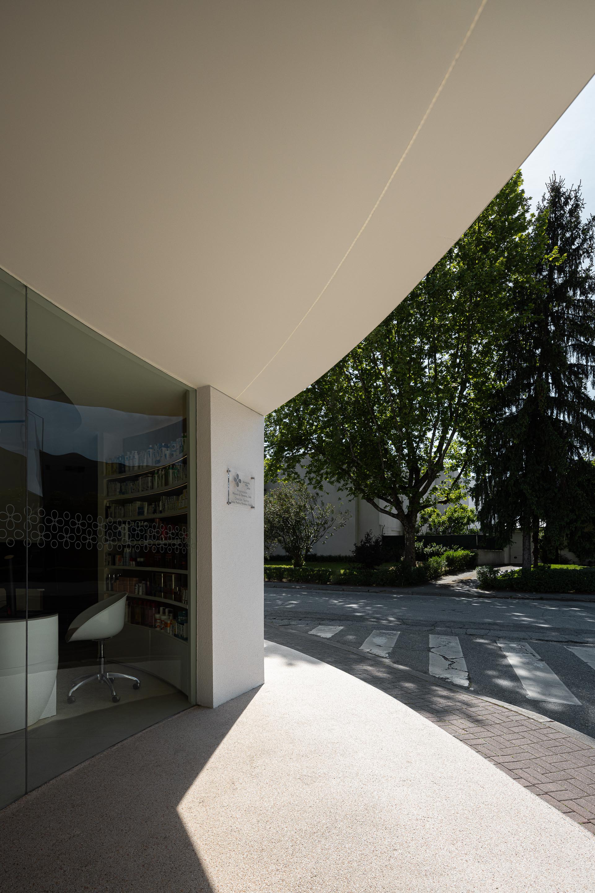 Entrada envidraçada com cobertura em consola curva, pavimento em mármore de Estremoz jateado e vegetação exterior — Farmácia São João arquitectura Tsou Arquitectos fotografia Ivo Tavares
